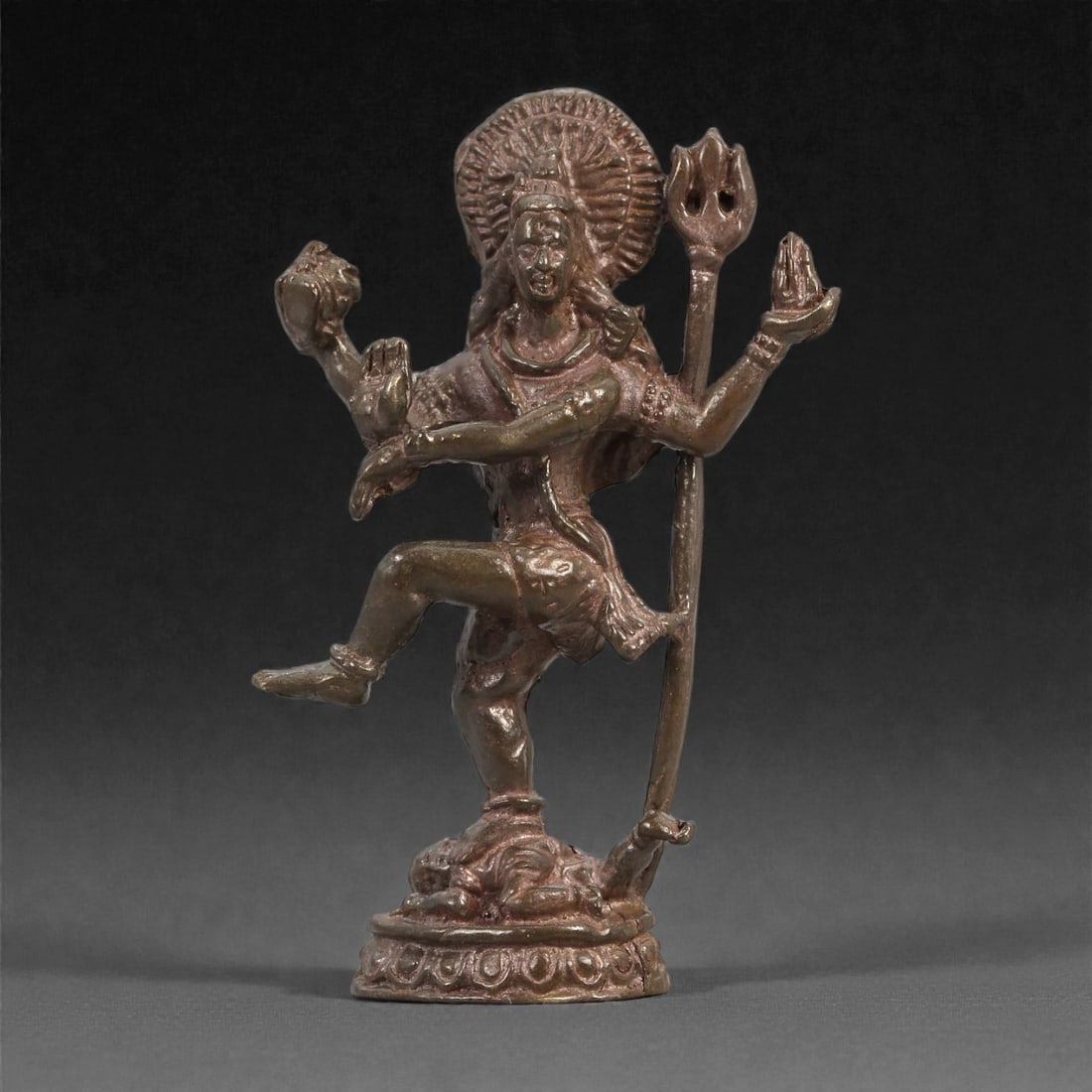 Bronze Dancing Deity with Trident - Hindu Icon Figurine, 8D: Cast in bronze with a warm, subtly reflective surface, this sculpture depicts a dynamic dancing deity poised upon a lotus-form base. The figure lifts one leg in an animated stride while the multiple a