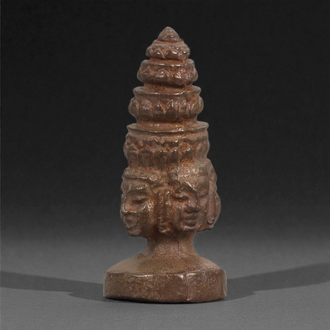 Bronze Four-Faced Miniature Idol - South Asian Figurine, 10D: Cast in bronze with a dense, finely grained surface, this miniature object presents a vertical columnar form crowned by a tiered conical headdress. Four stylized faces encircle the central shaft, each