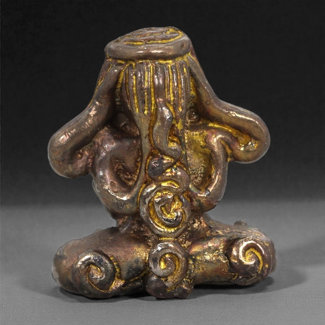 Bronze Abstract Seated Idol - South Asian Symbolic Figurine, 17D: Cast in bronze with a warm, unevenly lustrous surface, this miniature sculpture presents an abstract seated figure composed of curling, spiral-like forms that rise into elongated arm shapes framing th