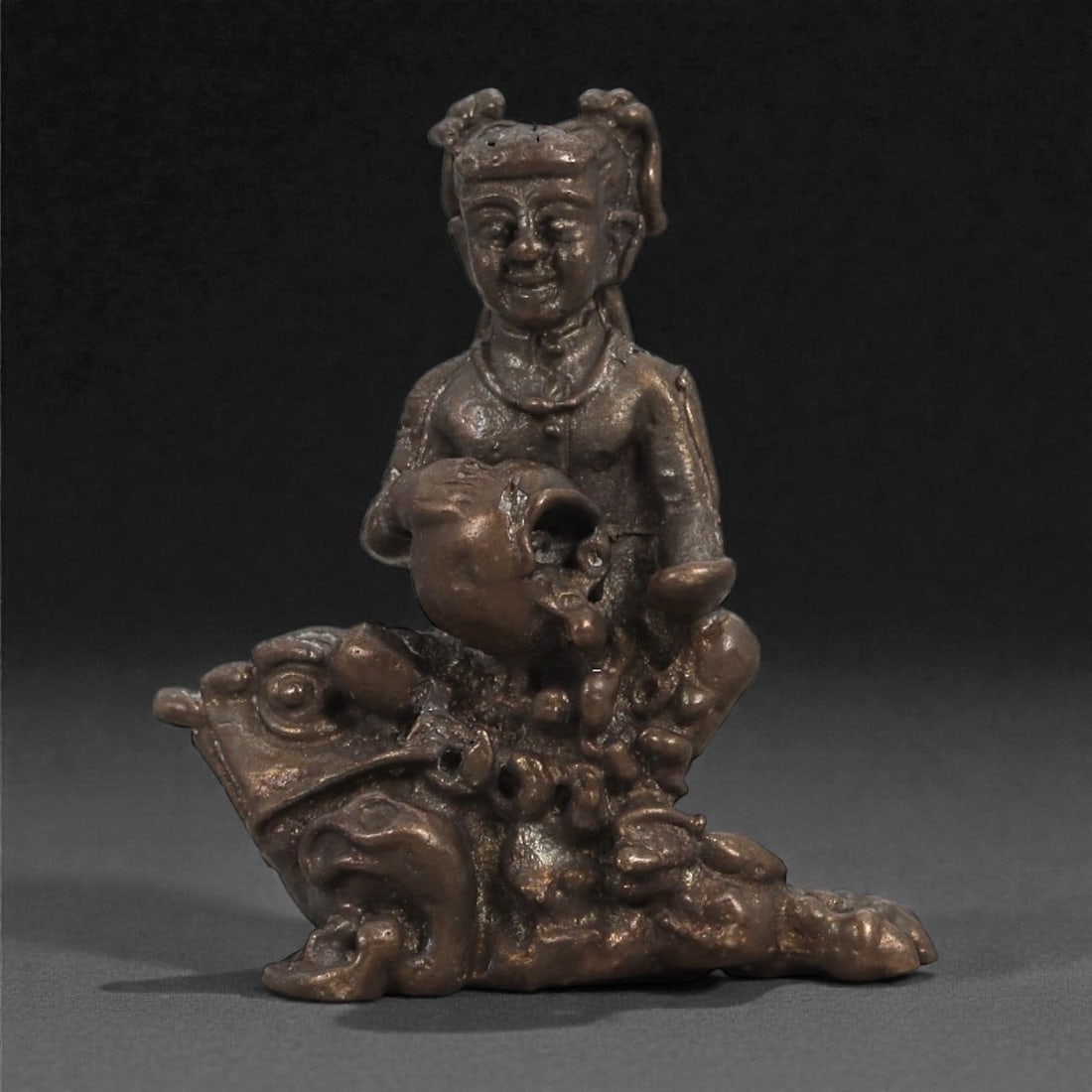Bronze Figure with Vessel on Mythic Beast - East Asian Figurine, 7D: Cast in bronze with a smooth, darkened surface, this small sculpture depicts a seated figure holding a rounded vessel while positioned atop a stylized mythic beast. The human figure is rendered with a