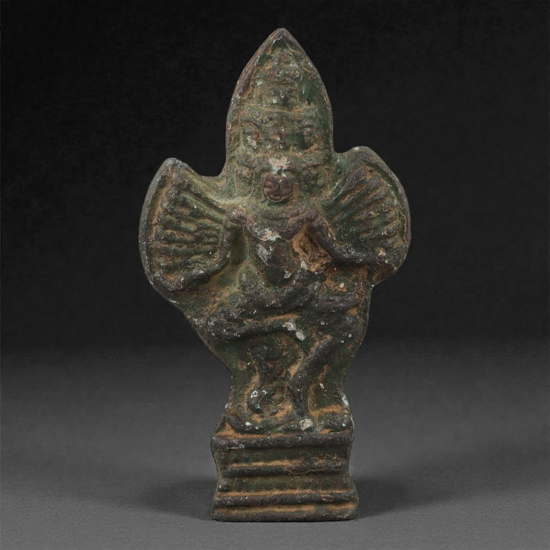 A Khmer Copper Alloy Garuda Plaque, Angkor Period, 12th-13th Century, 5LS: Cast in copper alloy with a dark green patina and areas of earthen accretion, the plaque depicts Garuda standing atop a tiered base, the wings outstretched and the arms bent forward in grasping postur