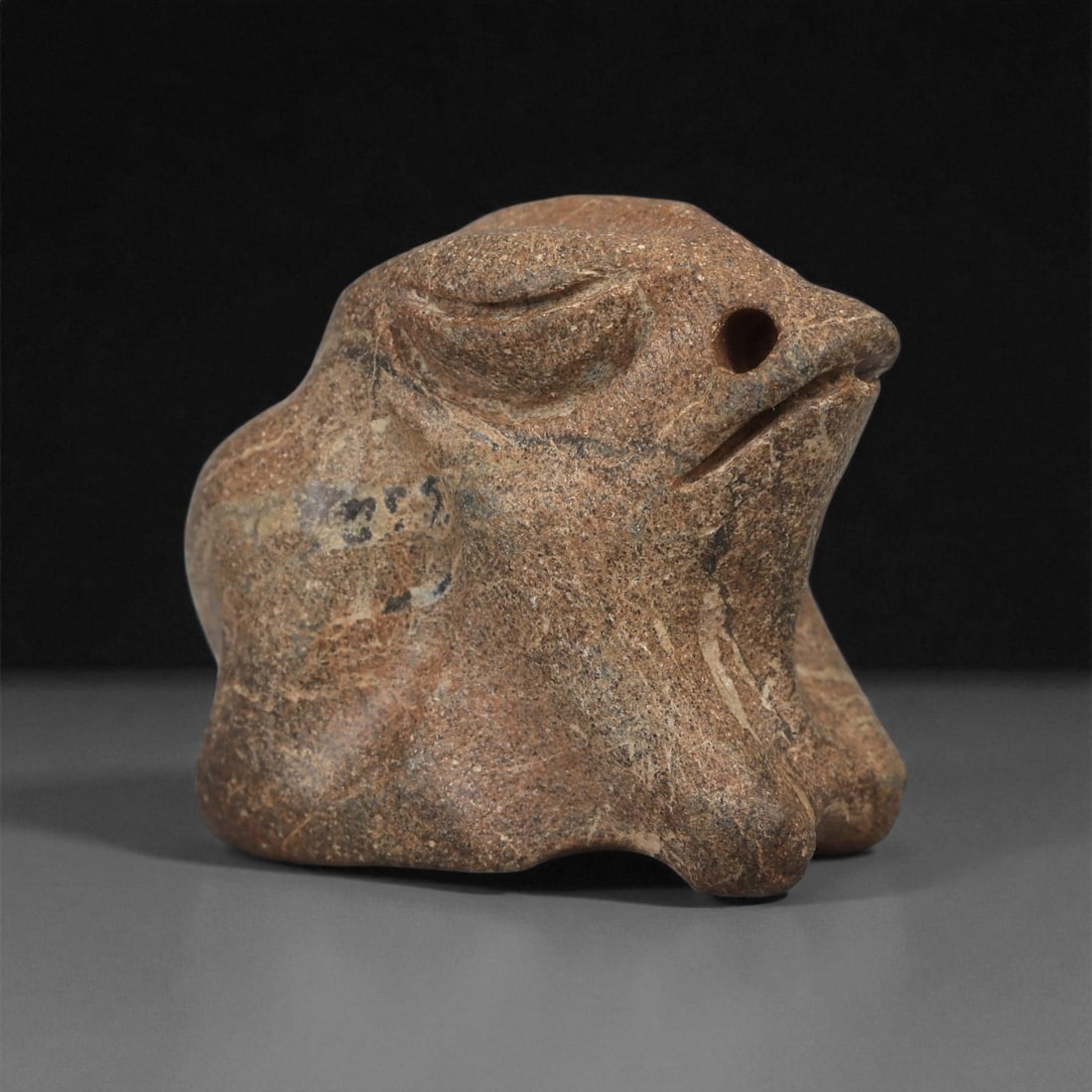 A Near Eastern Stone Amphibian Figurine, 3rd-2nd Millennium BCE, 74LA: Carved from a mottled brown stone with surface veining, the figure is modeled with a compact, crouching body supported on four splayed limbs. The head projects forward with a rounded snout, a single d