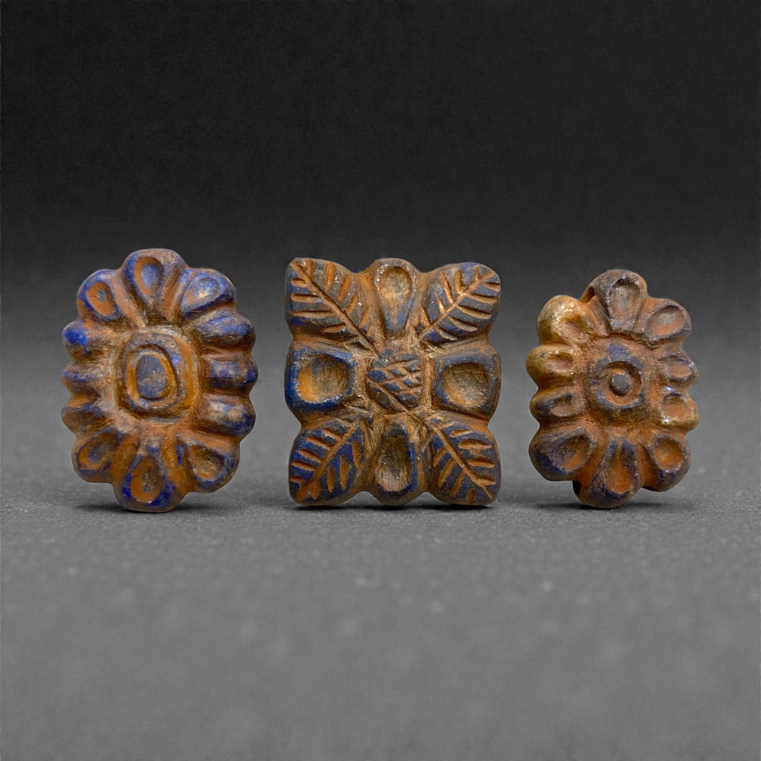 A Group of Three Achaemenid Lapis Lazuli Floral Beads, 5th-4th Century BCE, 92AA: Carved from deep blue lapis lazuli with natural inclusions, each bead is worked in a stylized floral form, comprising either radiating petals or a quadripartite rosette with incised leaf motifs. The r