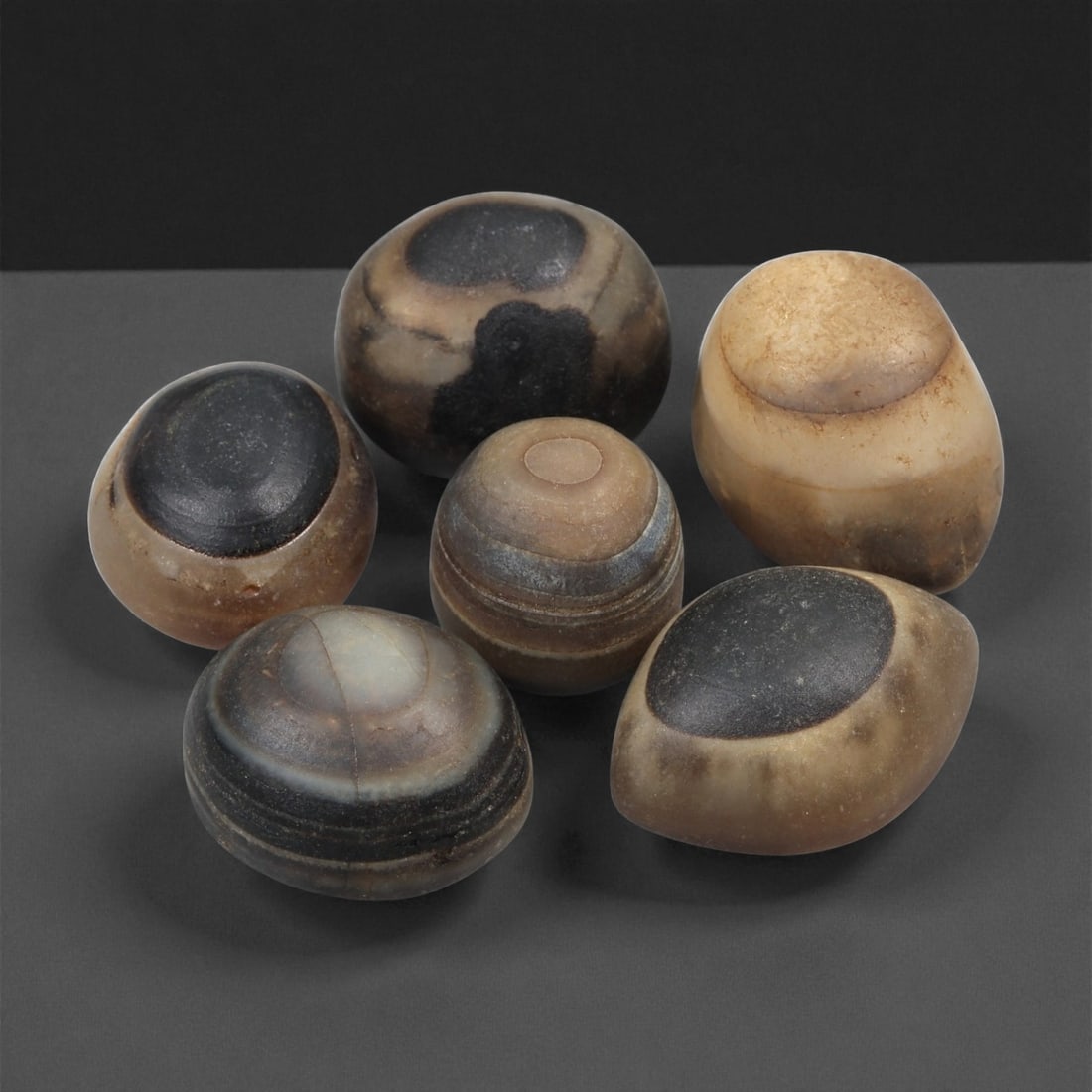 A Group of Tibetan Stone Luk Mik ("Goat Eye") Beads, 19th-Early 20th Century, 31LG: Carved from banded agate and chalcedony, the group comprises six domed, oval, and lenticular beads characterized by concentric circular banding that creates the "eye" motif associated with luk mik for