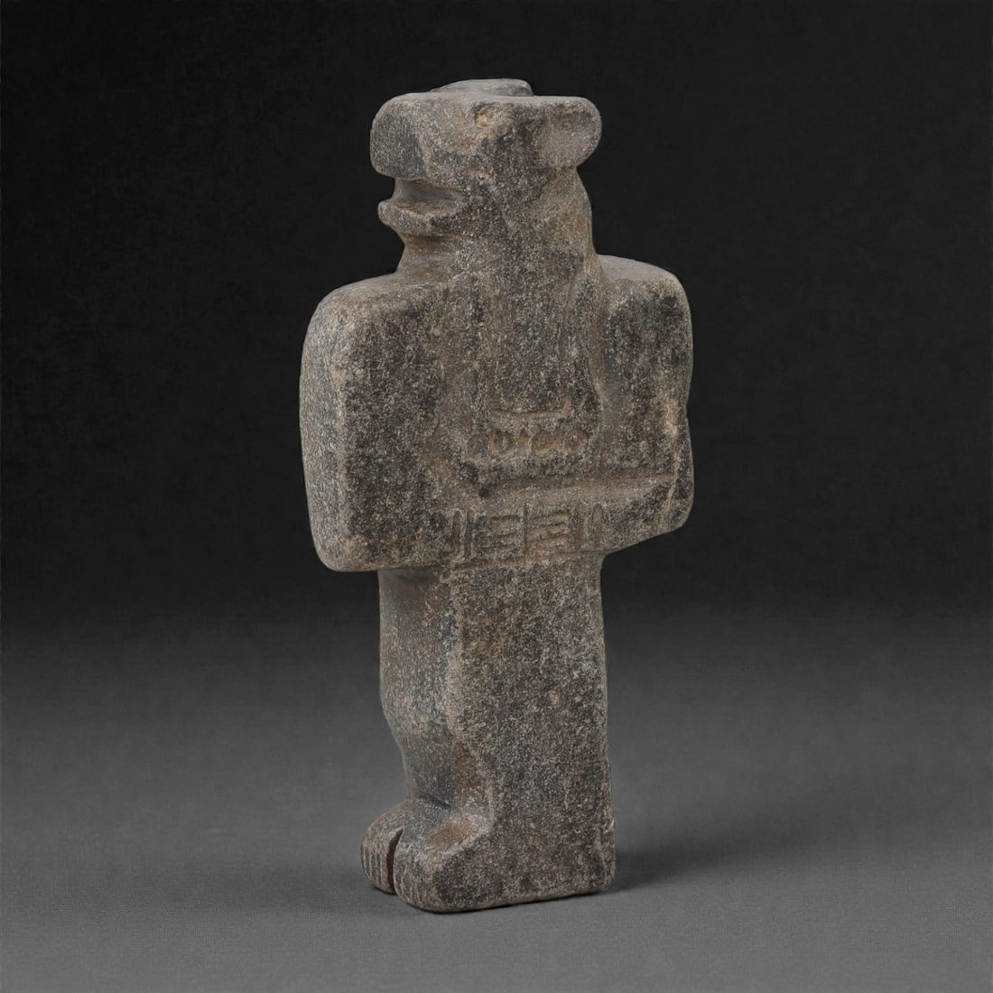 A South Arabian Grey Stone Anthropo-Zoomorphic Figure, 1st Millennium BCE, 7LM: Carved from a dark grey stone with a fine granular surface, the figure is rendered in an upright stance with broad shoulders, short arms folded across the torso, and straight legs terminating in feet