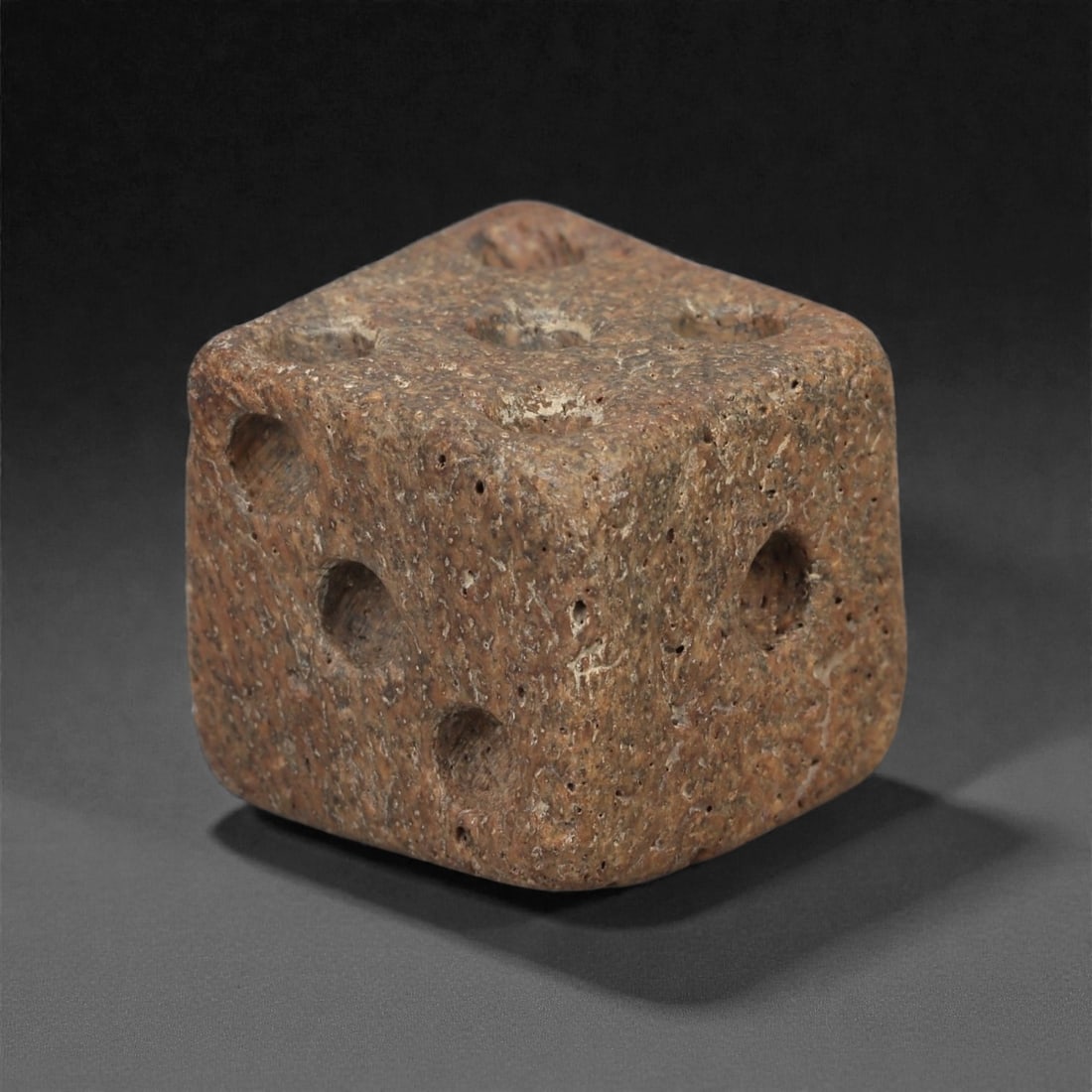 A Roman Bone Gaming Die, 1st-3rd Century CE, 1.3cm, 81AD: Carved from dense bone, the object is shaped as a small cube with slightly rounded edges. Each face bears a series of drilled circular pips arranged in standard numerical configurations. The surfaces 