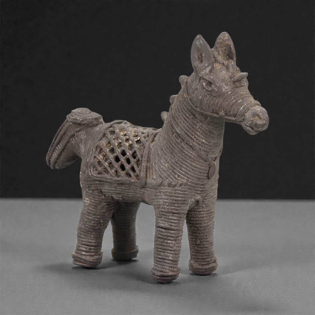 An African Bronze Horse Figure, 19th-Early 20th Century, 11LN: Cast in bronze by the lost-wax process, the figure depicts a standing horse with short cylindrical legs encircled by uniform linear grooves. The elongated head is rendered with upright ears, a slightl