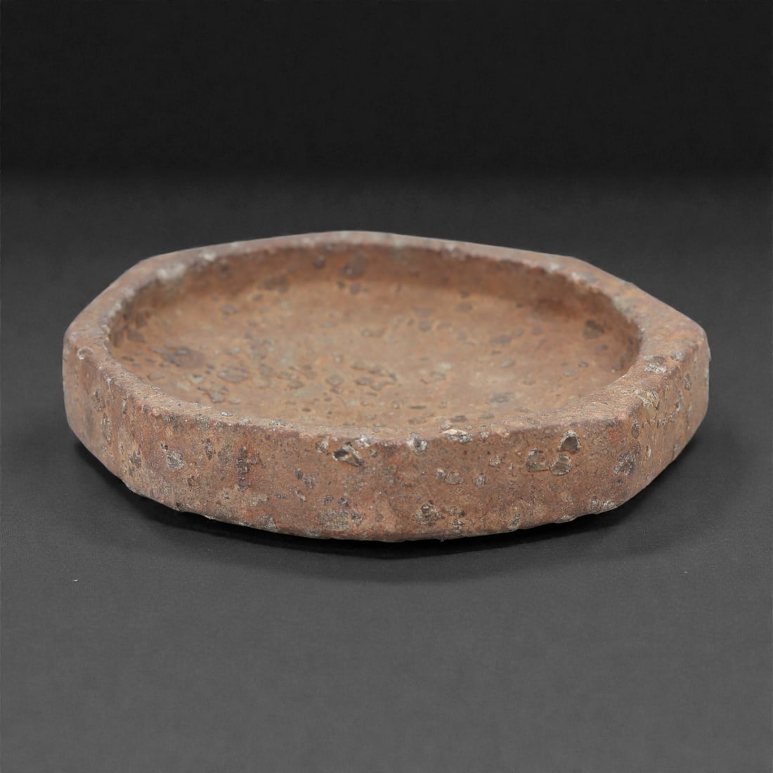 A Mesopotamian Stone Dish, Iron Age, 1st Millennium BCE, 38LR: Carved from a coarse-grained stone with a worn brown archaeological surface, the object is shaped as a shallow circular dish with a slightly raised rim and a flattened base. The interior is smoothly h