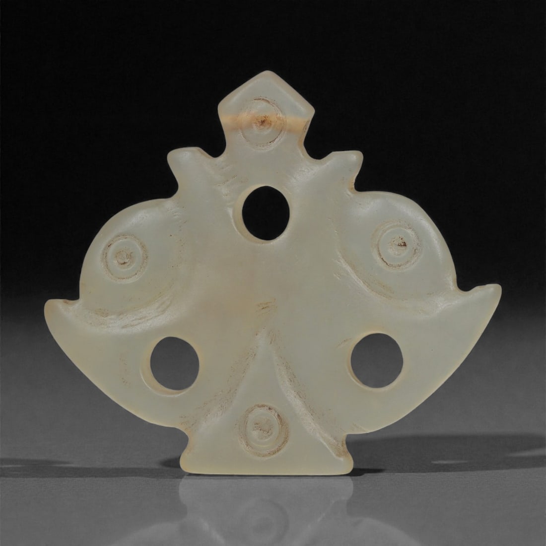 An Islamic Jade Openwork Plaque, Medieval Period, 12th-14th Century CE, 90LP: Carved from translucent pale green jade, the plaque is shaped in a symmetric, fan-like contour with broadly flaring lateral lobes and a small stepped upper finial. Four circular perforations are drill