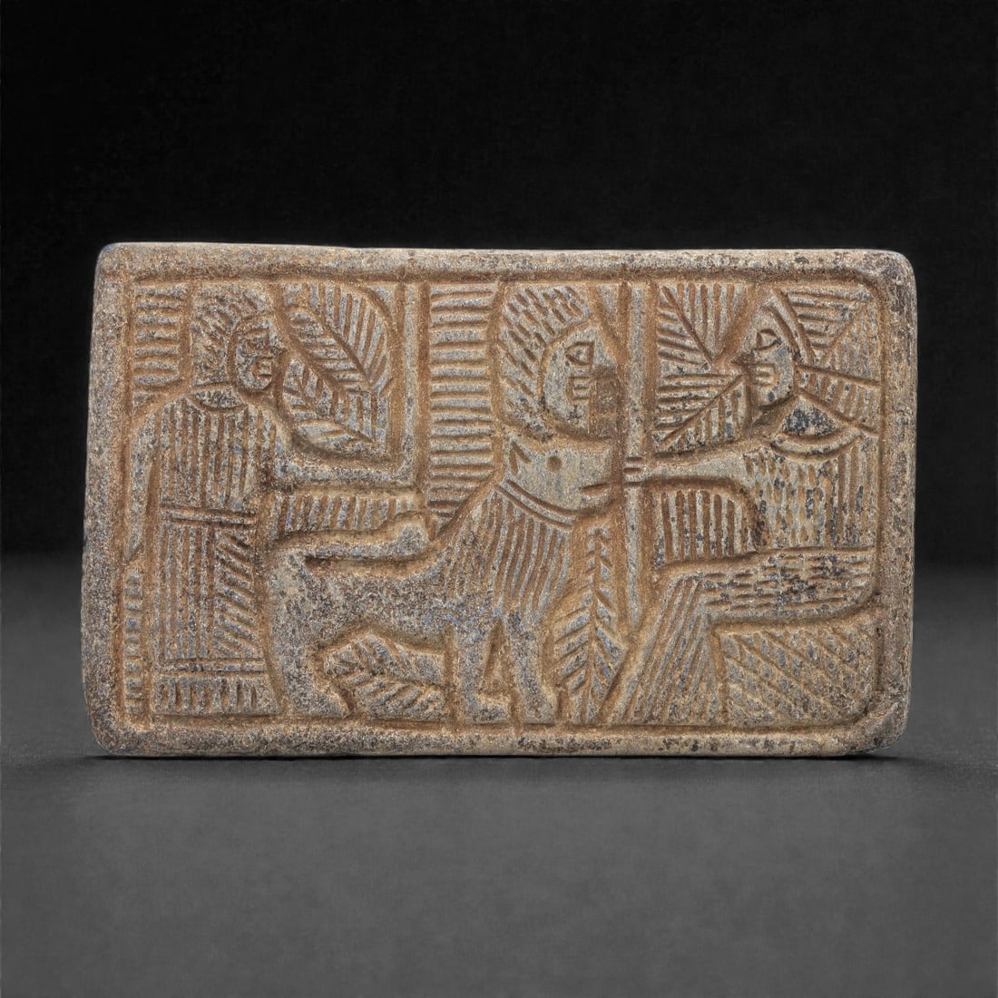 A Sasanian Lapis Lazuli Relief Plaque, 3rd-7th Century CE, 9.8cm, 59LQ: Carved from lapis lazuli with brown archaeological surface accretions, the plaque is worked in shallow relief exhibiting the characteristic linear incision and patterned surface treatment associated w