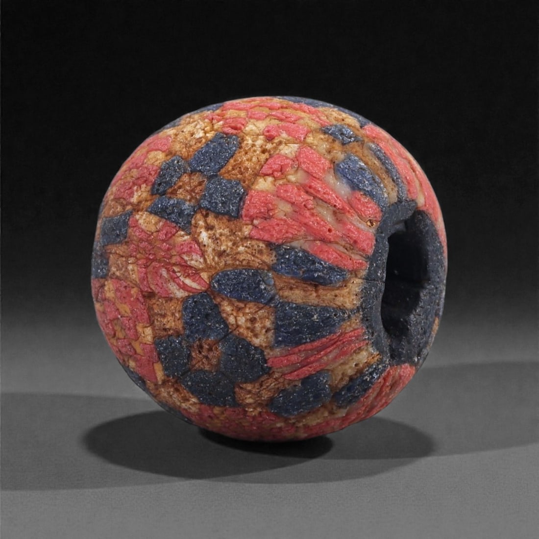 Ancient Egypto-Roman Mosaic Glass Bead - Millefiori Checker Pattern Sphere, 41J: Constructed from richly colored mosaic glass, this spherical bead is composed of densely arranged millefiori cane slices in red, dark blue, and warm beige tones. The canes have been fused and ground i