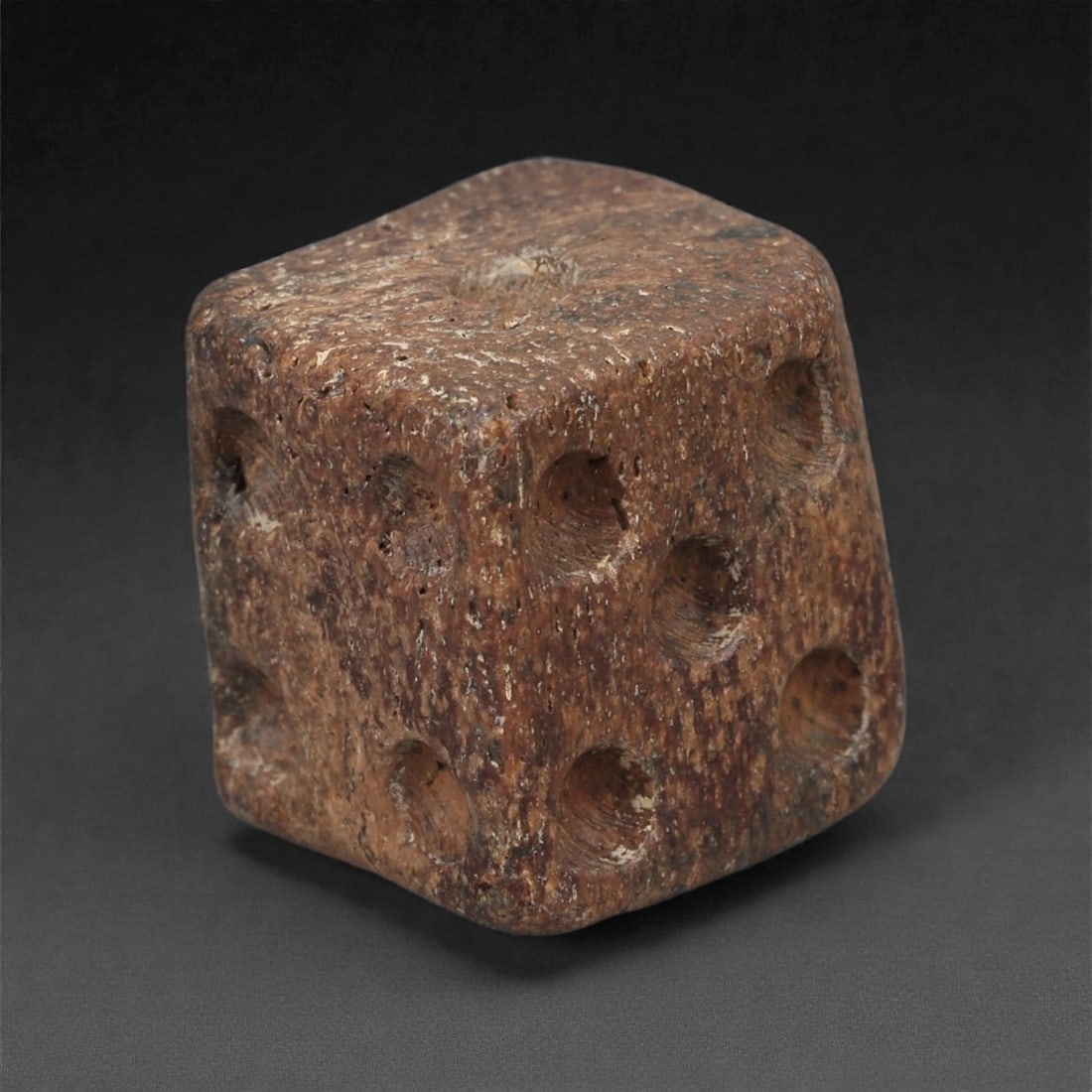 A Roman Bone Gaming Die, 1st-3rd Century CE, 1.3cm, 78AD: Carved from dense bone, the object is shaped as a small cube with slightly rounded edges. Each face bears a series of drilled circular pips arranged in standard numerical configurations. The surfaces 