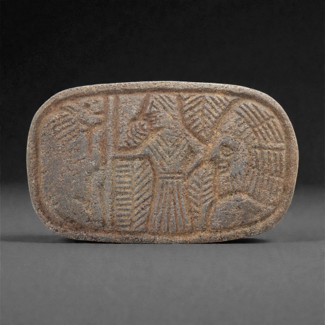 A Sasanian Lapis Lazuli Relief Plaque, 3rd-7th Century CE, 8.7cm, 93LQ: Carved from lapis lazuli with brown archaeological surface accretions, the plaque is worked in shallow relief exhibiting the characteristic linear incision and patterned surface treatment associated w