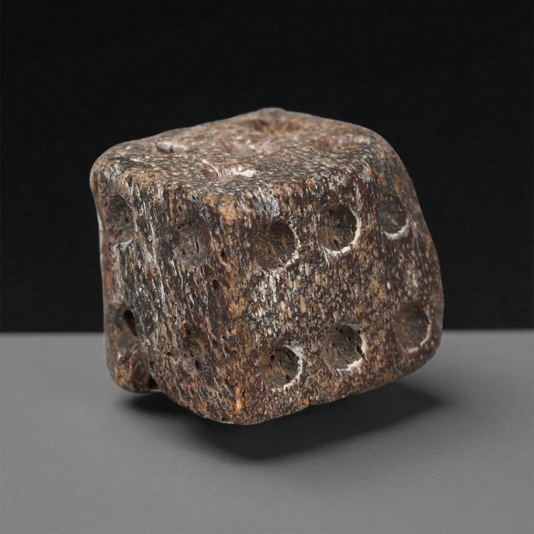 A Roman Bone Gaming Die, 1st-3rd Century CE, 1.6cm, 58ZA: Carved from dense bone, the object is shaped as a small cube with slightly rounded edges. Each face bears a series of drilled circular pips arranged in standard numerical configurations. The surfaces 