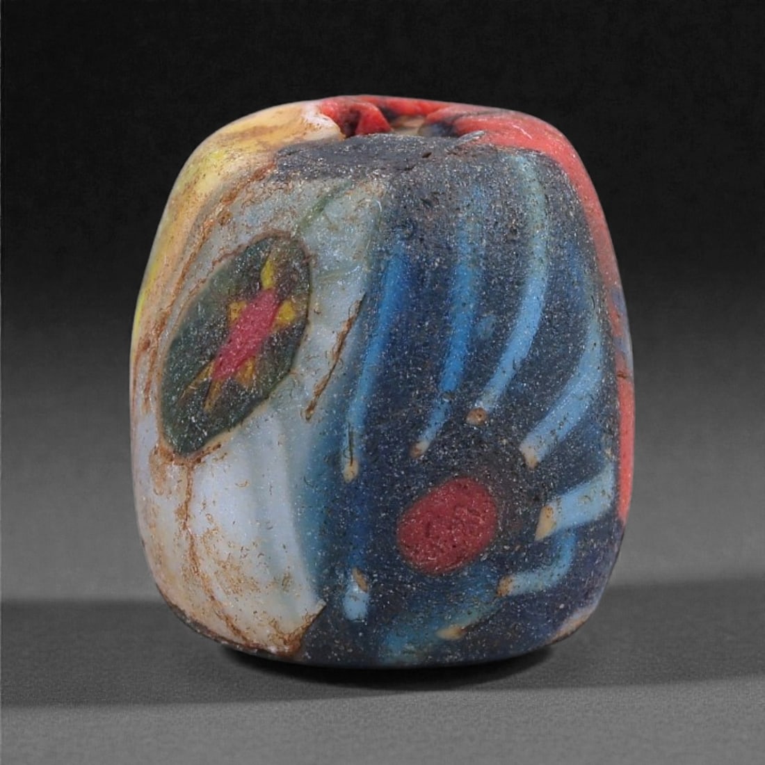 Ancient Egypto-Roman Swirled Mosaic Glass Bead - Multicolor Sphere, 28J: Fashioned in opaque mosaic glass, this small spherical bead is composed of tightly fused canes displaying dynamic marbled swirls in yellow, red, blue, and pale tones. The sinuous, flame-like patternin