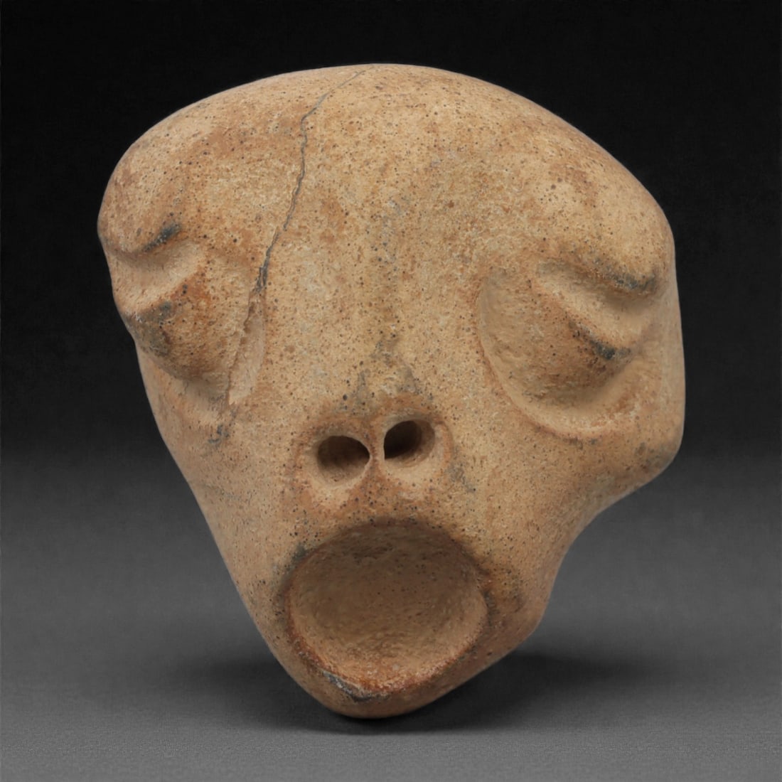 A Mediterranean Stone Maskette, 12th-17th Century, 41LQ: Carved from a light tan stone with fine granular texture, the maskette is shaped with a broad upper contour tapering into a narrow lower section. The facial features are rendered in shallow relief, in