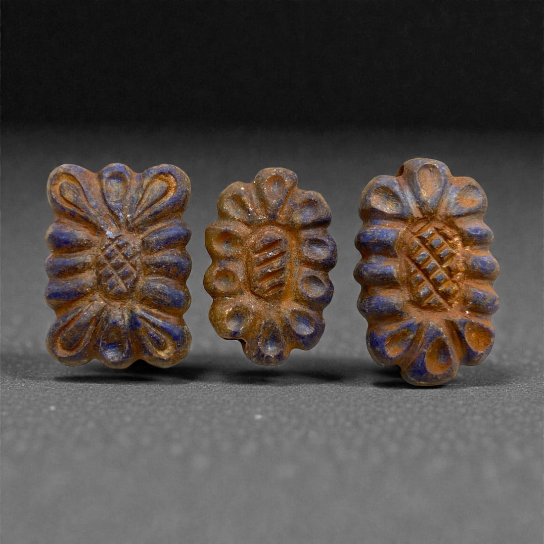 Achaemenid Lapis Lazuli Floral Beads, 5th-4th Century BCE, 93AA: Carved from deep blue lapis lazuli with natural pyrite inclusions, the three beads are shaped as stylized rosettes with a central oval field bearing incised diagonal cross-hatching. Each bead is borde