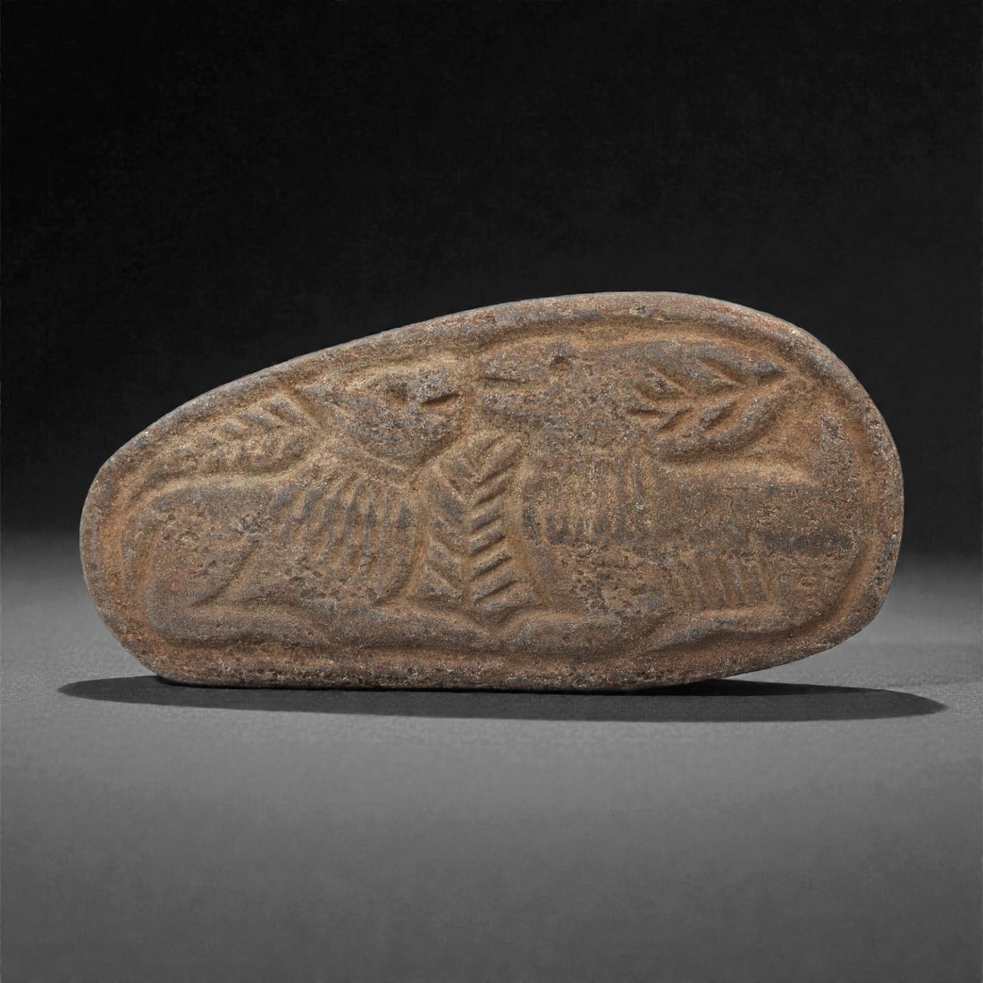 A Sasanian Lapis Lazuli Relief Plaque, 3rd-7th Century CE, 7.7cm, 61LQ: Carved from lapis lazuli with brown archaeological surface accretions, the plaque is worked in shallow relief exhibiting the characteristic linear incision and patterned surface treatment associated w