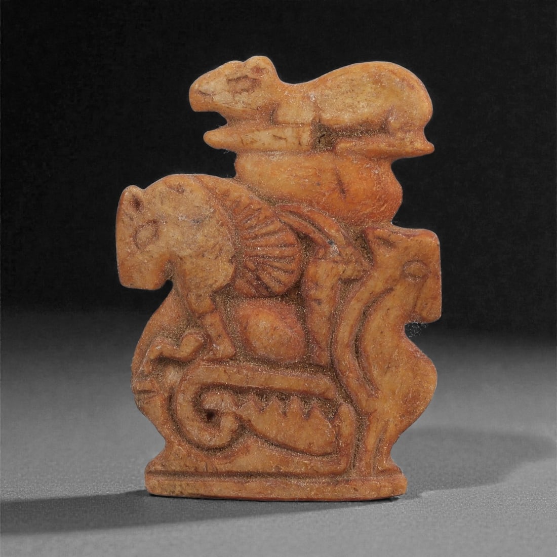 A Parthian Carved Bone Plaque with Animal Motifs, 1st-3rd Century CE, 5LJ: Carved from a light brown bone with darker accretions in recessed areas, the plaque presents a complex arrangement of zoomorphic figures in low relief. The central register shows a horse-like animal w