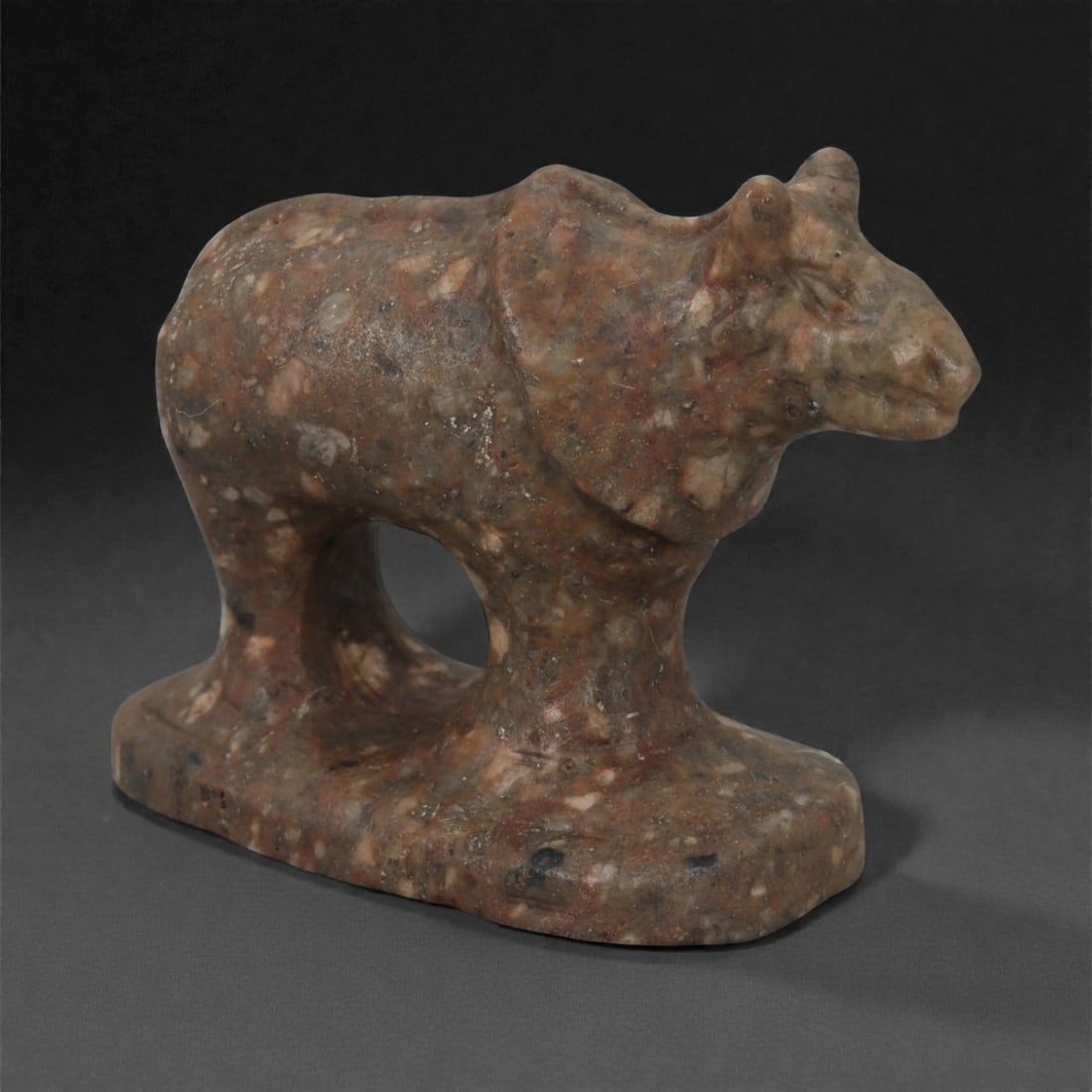 An Indo-Parthian Stone Bovid, 1st Millennium CE, 41LF: Carved from a mottled brown stone with lighter inclusions, the figure depicts a standing bovid on an integral rectangular base. The body is modeled with broad, rounded forms, a pronounced arch between