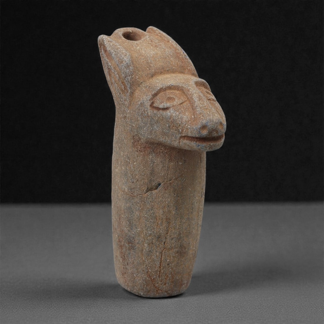 A Parthian Lapis Lazuli Feline-Head Amulet, 1st Century BCE-2nd Century CE, 52LR: Carved from lapis lazuli bearing brown archaeological surface accretions, the amulet is shaped as an elongated cylindrical body surmounted by a stylized feline head. The head is defined by upright ear