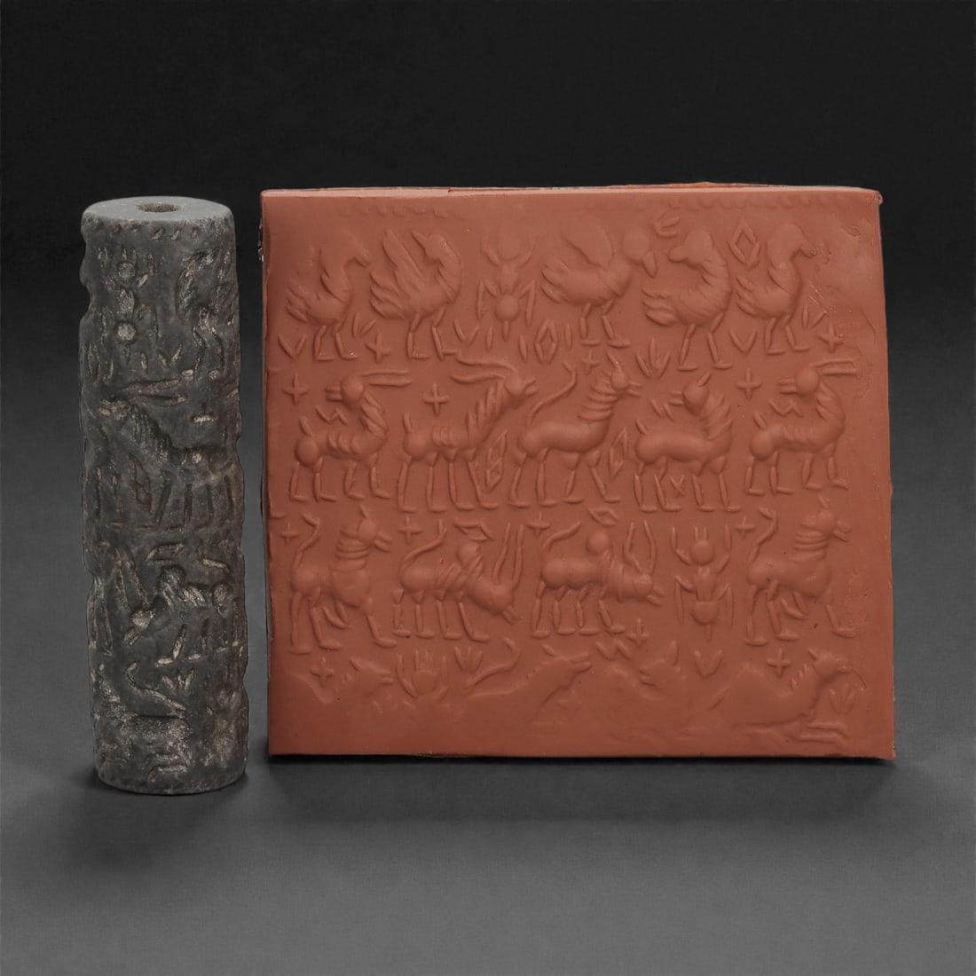 A South Arabian Steatite Cylinder Seal with Rows of Animals, 1st Millennium BCE, 93LN: Carved from dark grey steatite, the tall cylindrical seal bears three horizontal registers of incised animal figures. The composition includes birds with outstretched wings, caprids and horned quadrup