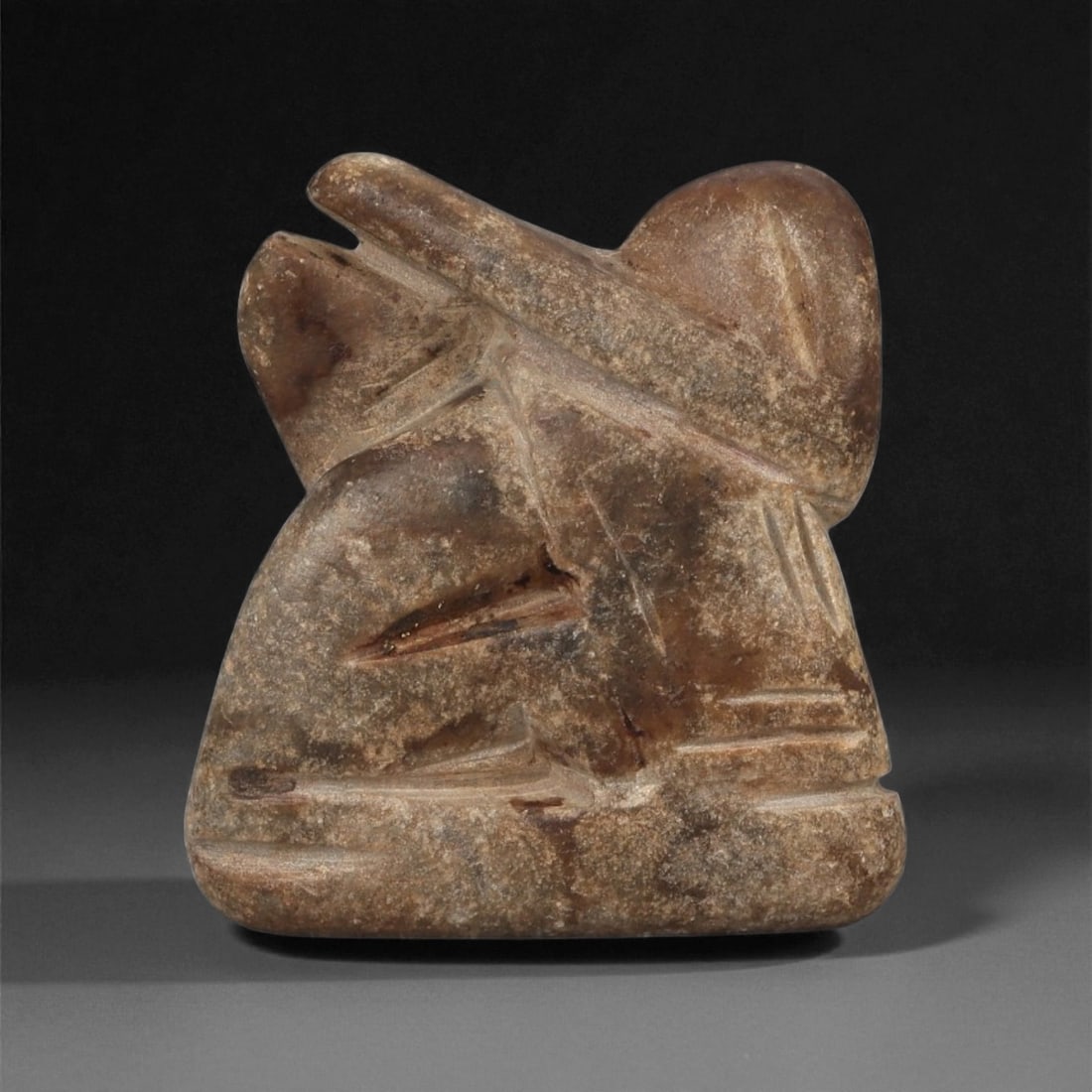 A Near Eastern Stone Griffin Effigy, 3rd-2nd Millennium BCE, 93LE: Carved from a brown stone with natural surface mottling, the object represents a compact griffin shown in a recumbent posture. The head is avian, with a projecting beak and a rounded crest, while the 