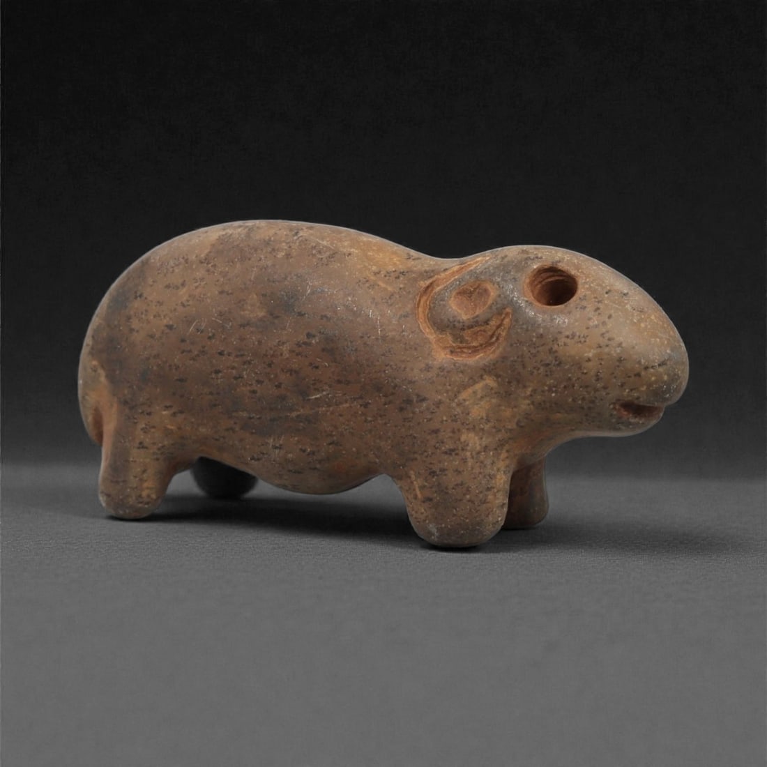 A Near Eastern Stone Zoomorphic Figurine, 3rd Millennium BCE, 12LF: Carved from a brown stone with scattered surface inclusions, the object is shaped as a small quadruped with a rounded back and short legs. The head is defined by a drilled circular eye, a shallow open
