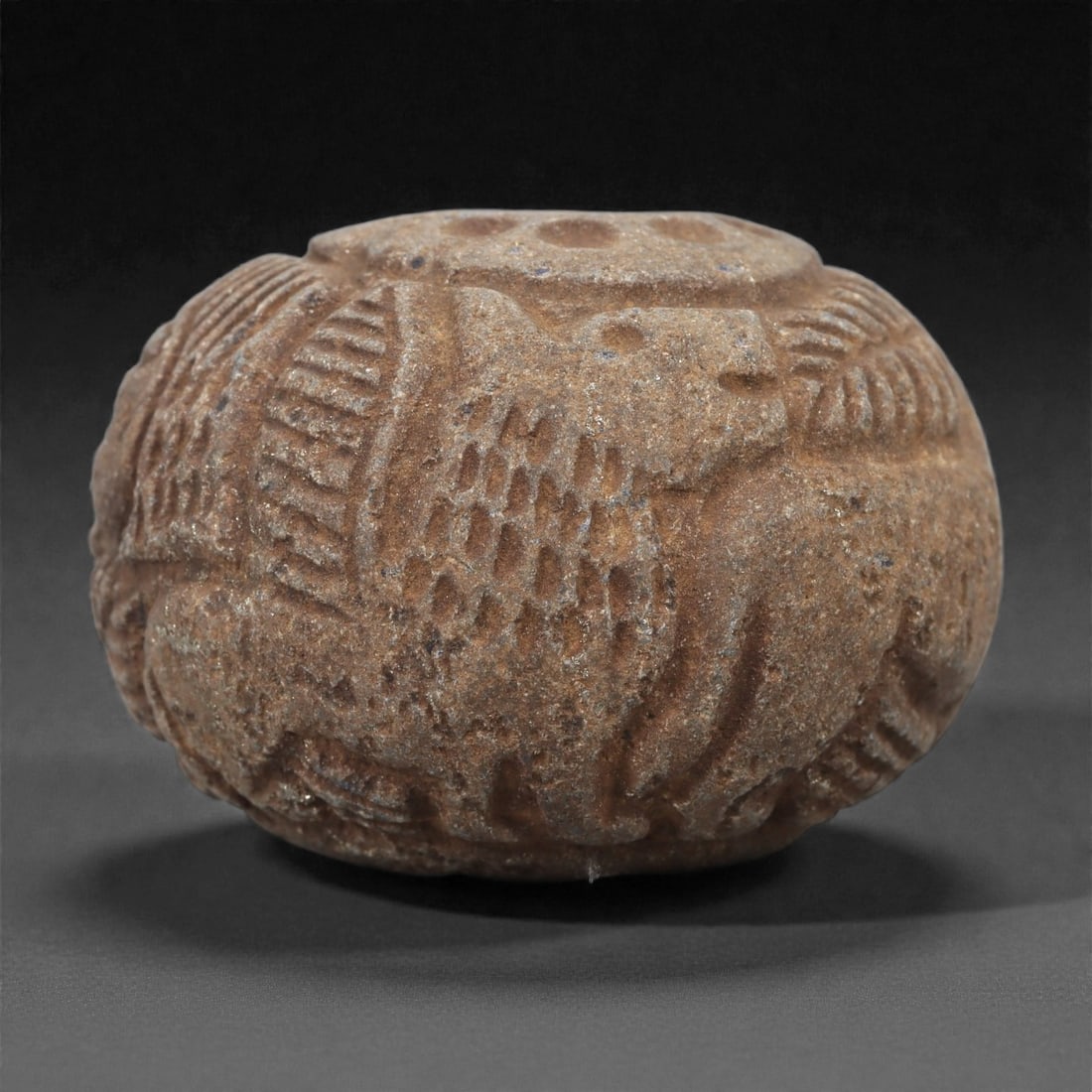 A Near Eastern (Achaemenid) Stone Bead with Winged Quadrupeds, 5th-4th Century BCE, 80LQ: Carved from a brown stone with lighter inclusions, the bead is shaped as a rounded, barrel-like form with a central perforation. The exterior is worked in low relief with a continuous frieze of winged