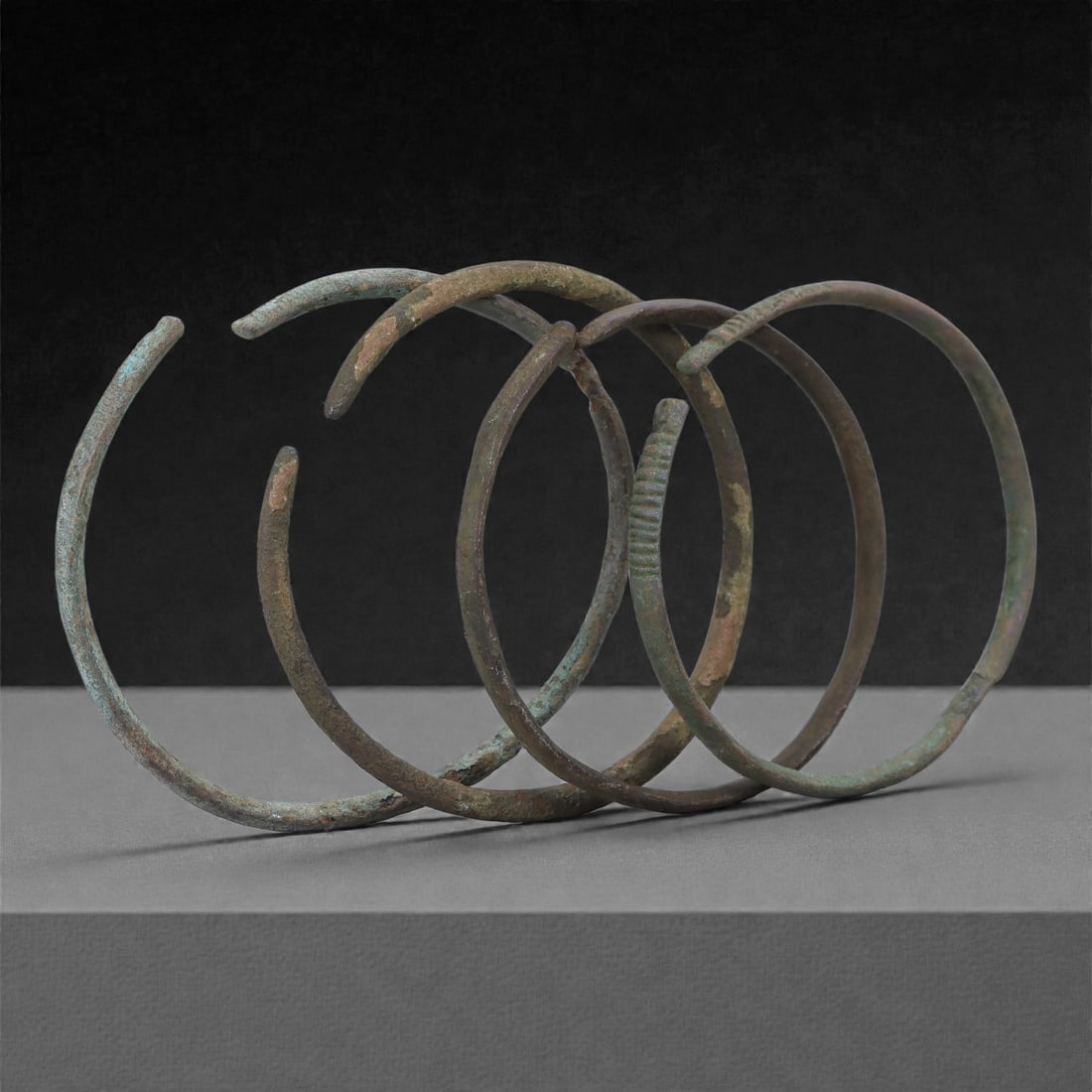Roman Bronze Bracelets, 1st-3rd Century CE, 10H: Cast in bronze with slender circular profiles, the group comprises four open bracelets exhibiting green and brown patination with localized surface accretions typical of burial conditions. Each bracel