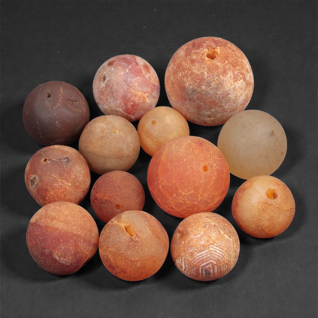 A Group of Tibetan Carnelian Beads, Early 20th Century, 1.2-2cm, 82LH: Comprising a group of spherical beads carved from orange to reddish-brown carnelian with natural banding and surface variation. Each is drilled longitudinally for stringing, consistent with traditiona