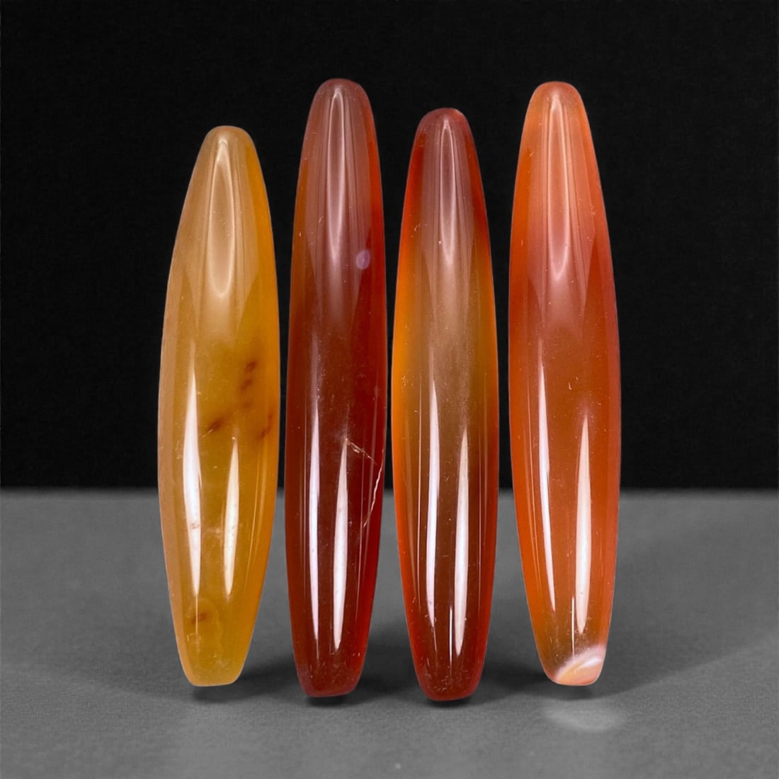 Tibetan Carnelian Ritual Beads, 19th-20th Century CE, 4.7-5.3cm, 7L: Carved from translucent orange carnelian with natural internal banding, the group comprises elongated, double-conical elements with smoothly polished surfaces. Each bead is unperforated, indicating a 