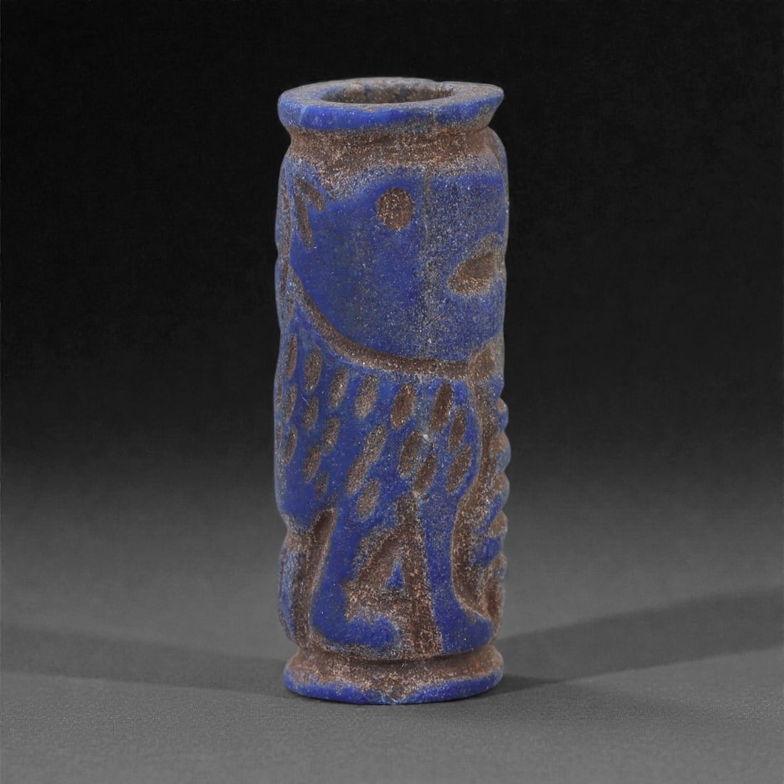 A Near Eastern Lapis Lazuli Cylindrical Relief Amulet, 3rd Millennium BCE, 3cm, 89L: Carved from lapis lazuli with mottled deep blue coloration interspersed with lighter calcite and brown mineral inclusions, the object is cylindrical in form with flat upper and lower faces. A longitud
