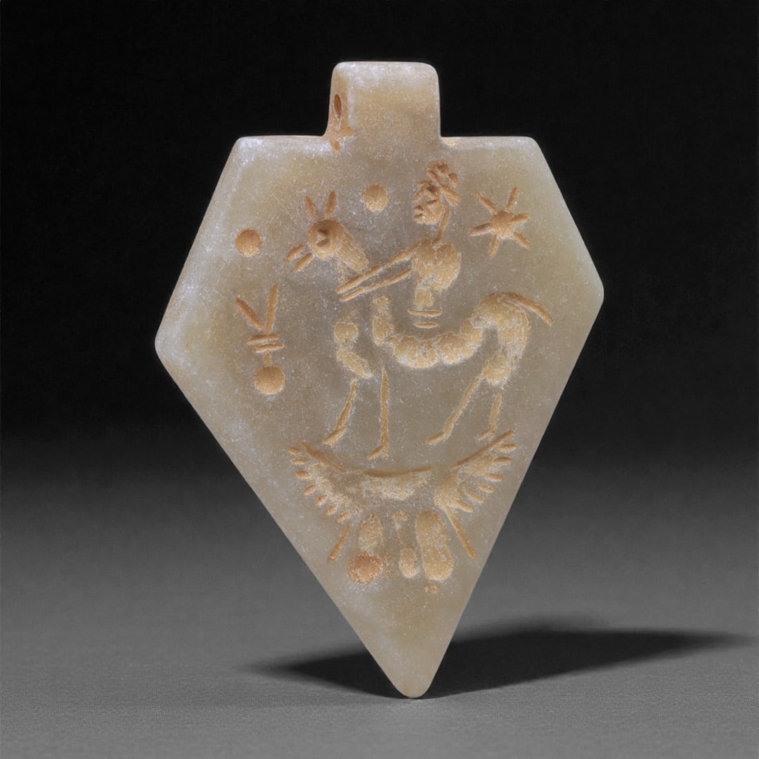 An Eastern Iranian Serpentine Amulet, Islamic Period, 9th-10th Century CE, 5cm, 82N: Carved from pale green serpentine with a smooth, slightly translucent surface, the object is worked in low relief on one face, with the reverse left plain and undecorated. The carved elements are defi