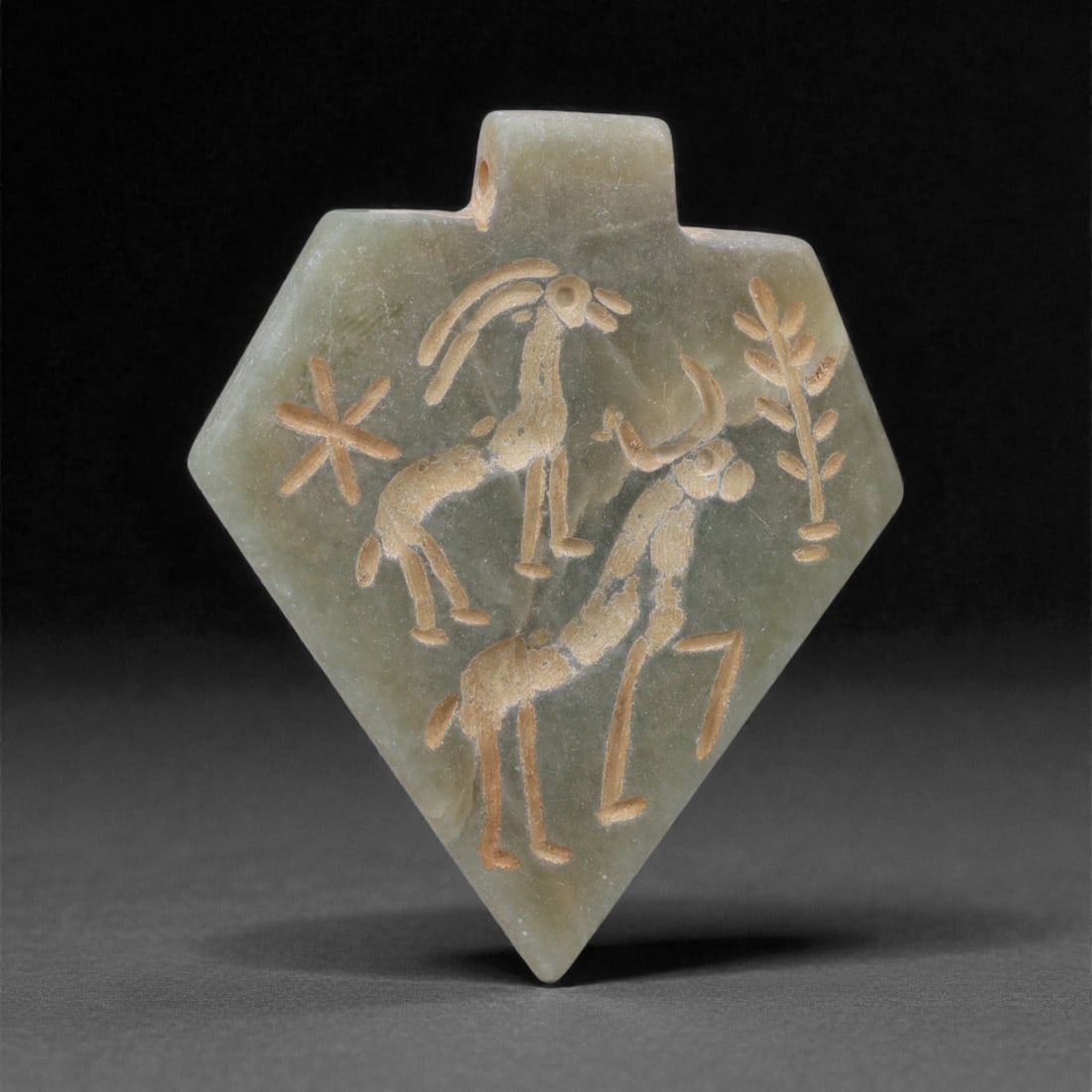 An Eastern Iranian Serpentine Amulet, Islamic Period, 9th-10th Century CE, 4.7cm, 3K: Carved from pale green serpentine with a smooth, slightly translucent surface, the object is worked in low relief on one face, with the reverse left plain and undecorated. The carved elements are defi