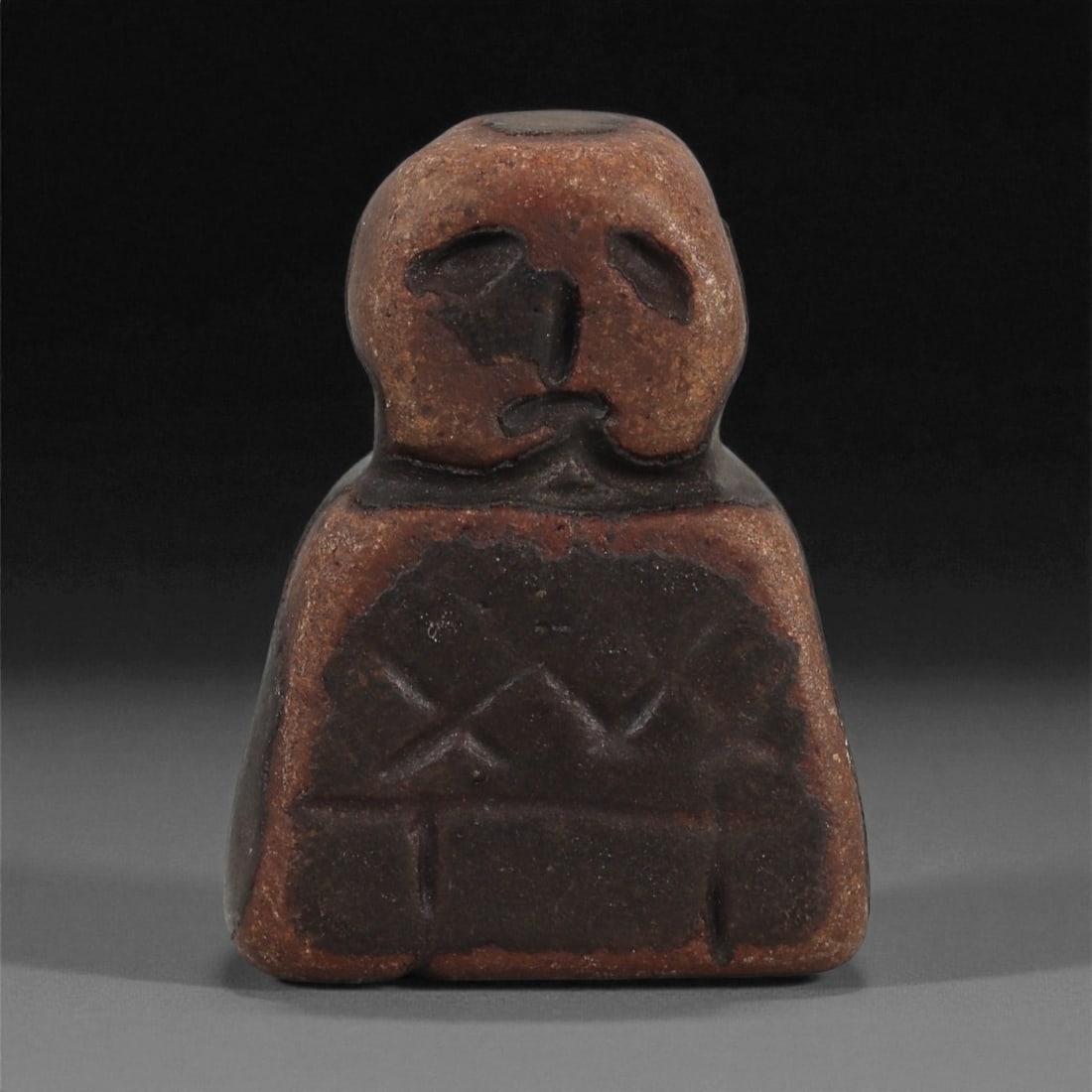 A Near Eastern Stone Anthropomorphic Idol, Early 1st Millennium BCE, 23AD: Carved from dark brown stone with a worn, smoothed surface, the idol is executed in a compact frontal form. The head is rounded and minimally articulated, with two shallow recessed eyes, a vertical in