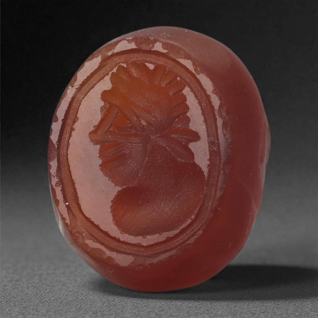 A Sasanian Carnelian Intaglio, 3rd-7th Century CE, 36LS: Carved from deep reddish carnelian, the gem is engraved in intaglio with a male bust in left profile. The figure wears a radiating headdress formed by a series of short linear strokes, with a banded e