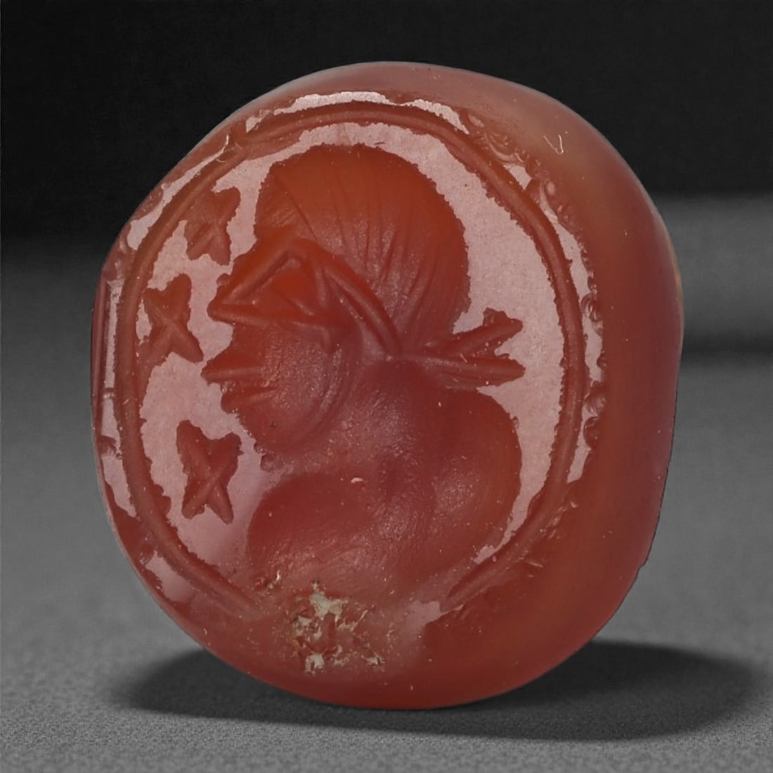 A Sasanian Carnelian Intaglio, 3rd-7th Century CE, 59LS: Carved from deep orange-red carnelian, the gem is engraved in intaglio with a male bust in left profile. The head is wrapped in a banded headdress, and the beard and facial contours are indicated with