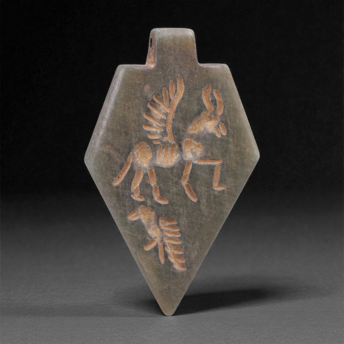 An Eastern Iranian Serpentine Amulet, Islamic Period, 9th-10th Century CE, 4.7cm, 94N: Carved from pale green serpentine with a smooth, slightly translucent surface, the object is worked in low relief on one face, with the reverse left plain and undecorated. The carved elements are defi