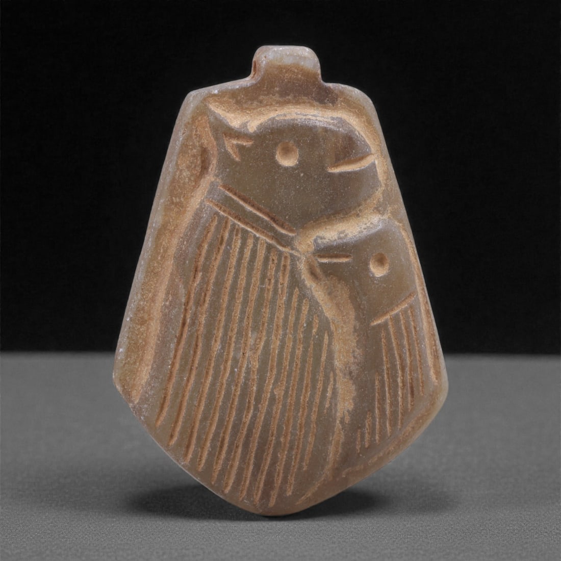 A Near Eastern Stone Bifacial Bird Amulet, Early 1st Millennium BCE, 76N: Carved from brownish-gray stone with lighter surface abrasion and areas of smoothing from use, the amulet is formed as a small tapering plaque with a flattened reverse and a short suspension tab at th