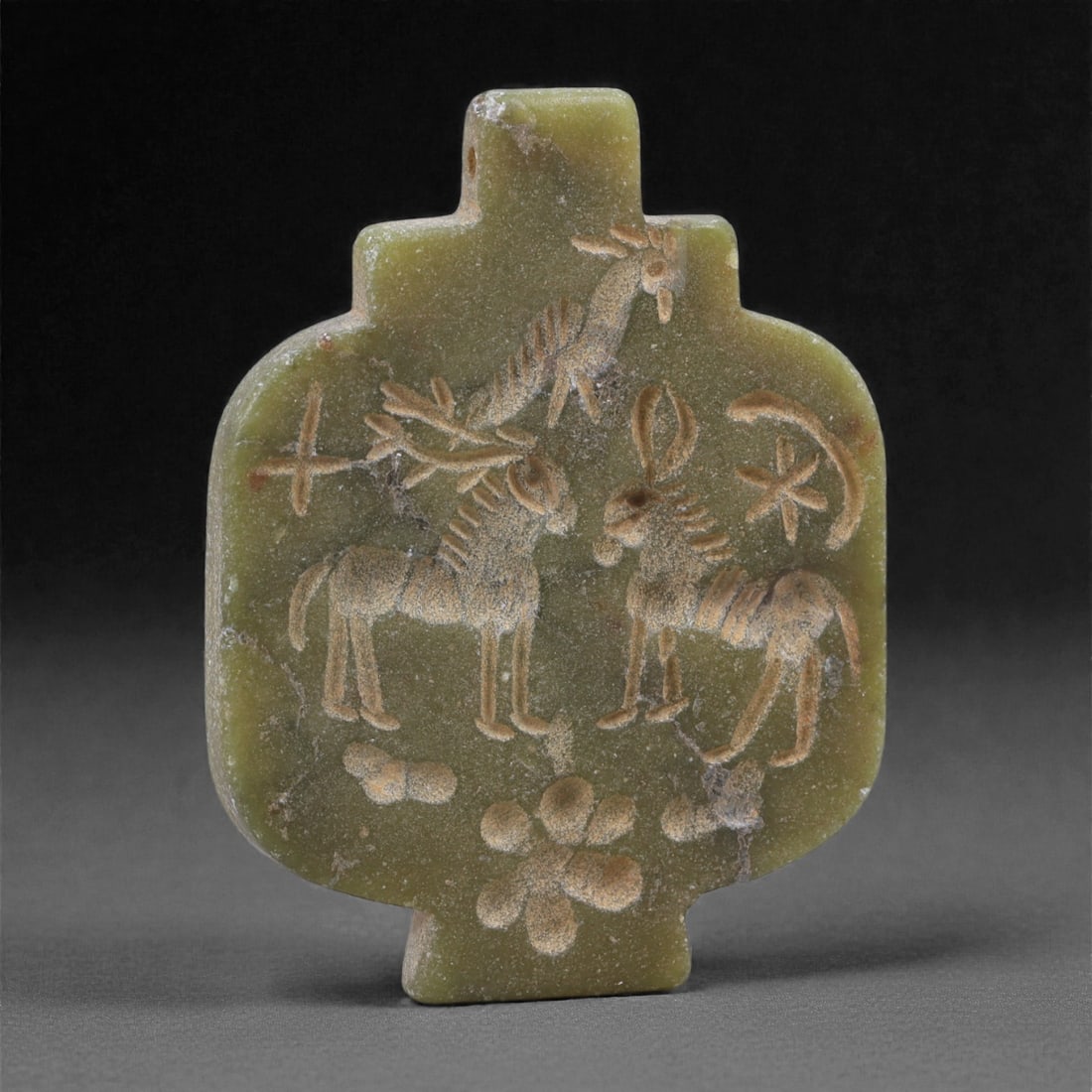 An Eastern Iranian Serpentine Amulet, Islamic Period, 9th-10th Century CE, 5.8cm, 75N: Carved from pale green serpentine with a smooth, slightly translucent surface, the object is worked in low relief on one face, with the reverse left plain and undecorated. The carved elements are defi