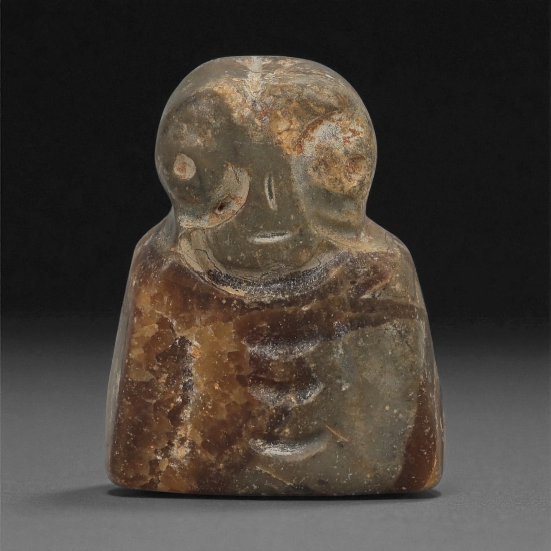 A Near Eastern Stone Anthropomorphic Figurine, 3rd-2nd Millennium BCE, 27LB: Carved from a brown and grey stone with translucent inclusions, the object depicts a stylized anthropomorphic figure with a broad head and large circular eyes formed by recessed rings. A short, incise