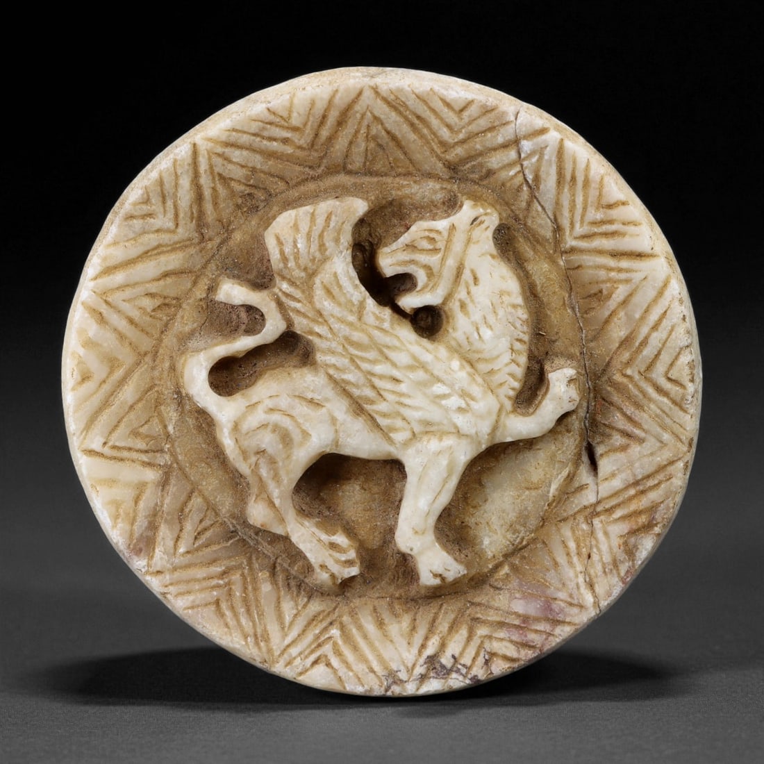 A Parthian Stone Roundel with Griffin Relief, 1st Century BCEEUR"1st Century CE, 2ER: Carved from a light beige stone with natural veining, the roundel bears a central relief depicting a griffin shown in profile with outstretched wings and a raised foreleg. The creature is framed withi