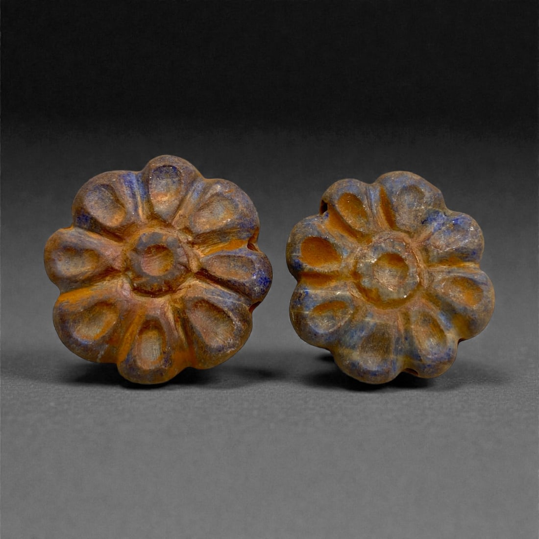 Achaemenid Lapis Lazuli Rosette Beads, 5th-4th Century BCE, 94AA: Carved from blue lapis lazuli with brown surface weathering, the two beads are shaped as circular rosettes composed of radiating rounded petals surrounding a slightly raised central disk. The reverse 