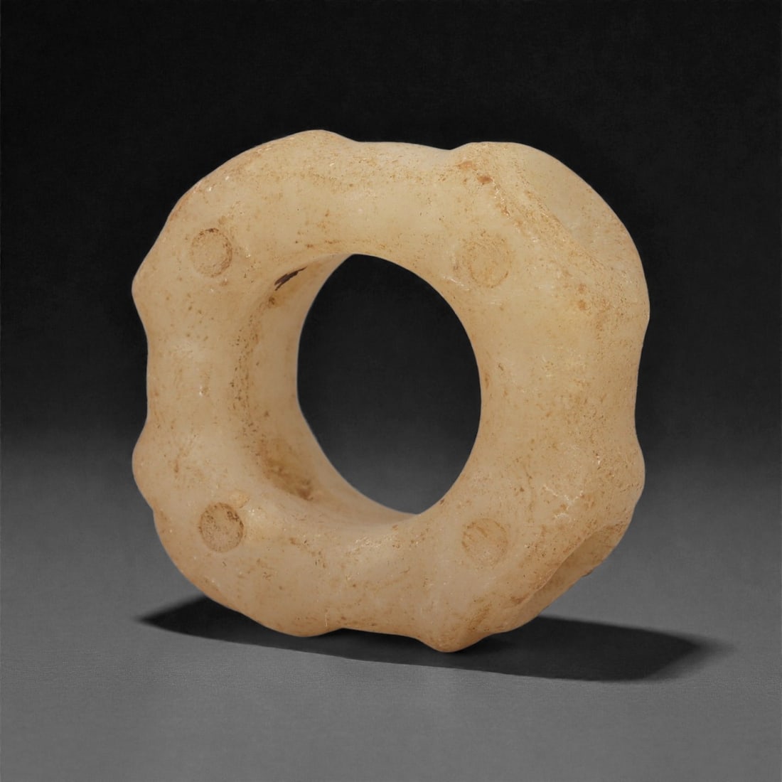 A Sino-Mongolian Jade Ring Bead, 1st Millennium BCE, 52LQ: Carved from pale jade with a smooth, matte surface, the bead is shaped as a circular ring with a broad, rounded cross-section. The outer perimeter is articulated by shallow scalloping, and four recess