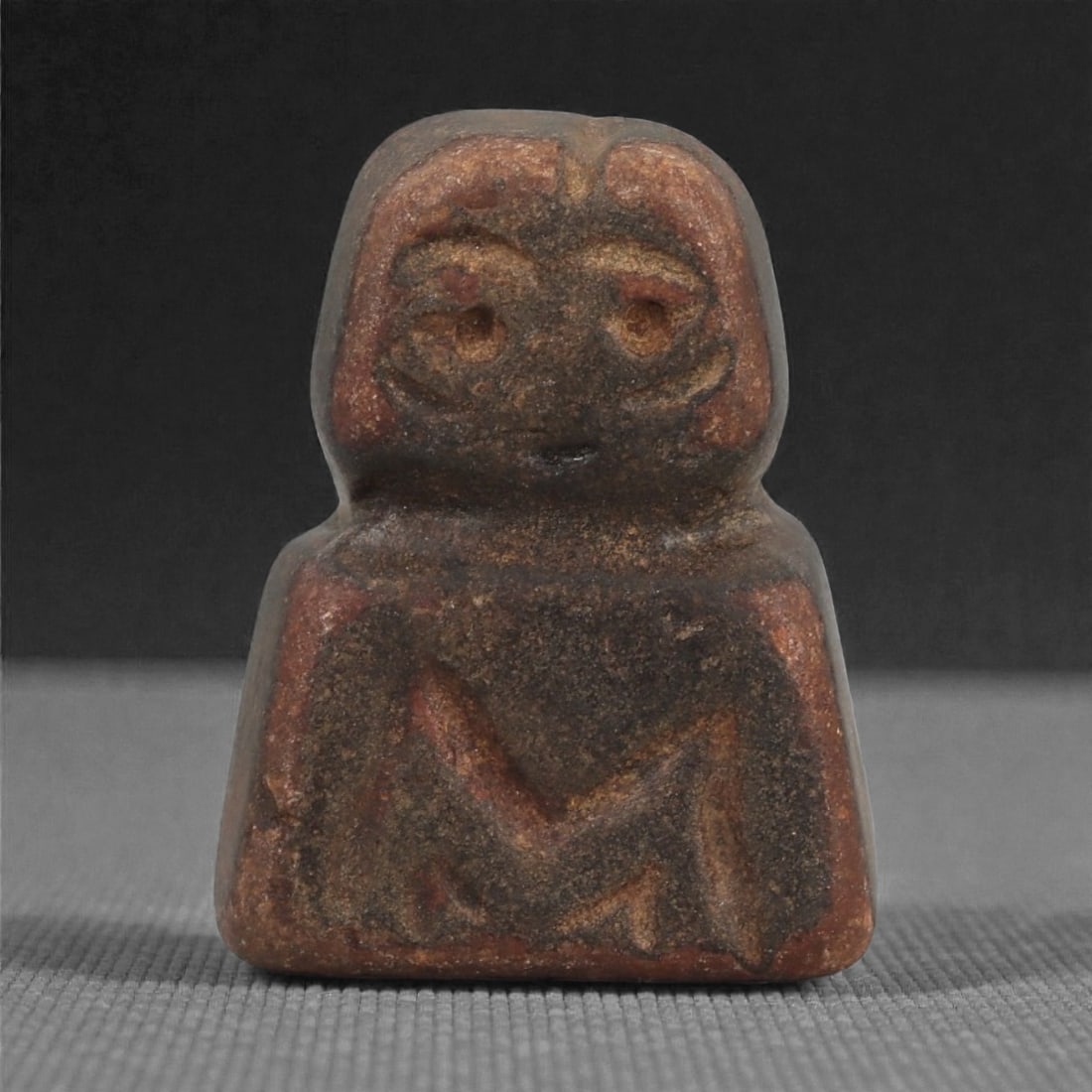 A Near Eastern Stone Anthropomorphic Idol, 11AD: Carved from dark brown stone with a smooth, worn surface, the idol depicts a compact frontally posed figure. The head is rounded, with shallow recessed eyes outlined by curved incised lines, a short v
