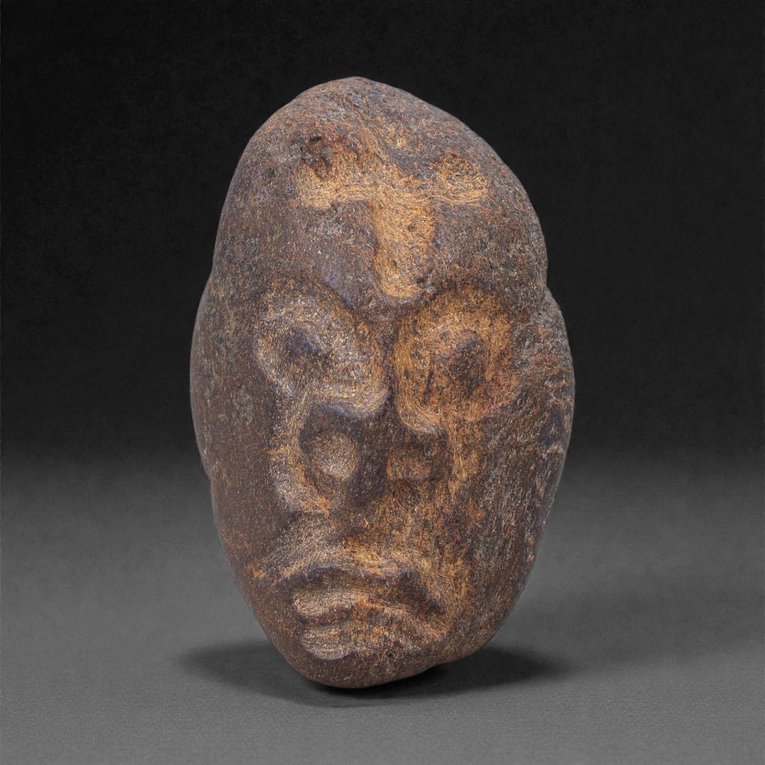 Ancient Fossil Bone Stone Anthropomorphic Face Effigy - Maskette Sculpture, 19F: This compact anthropomorphic effigy represents a stylized human face carved from dense fossilized bone stone. The form is elongated and mask-like, with softly rounded contours and a calm, introspectiv