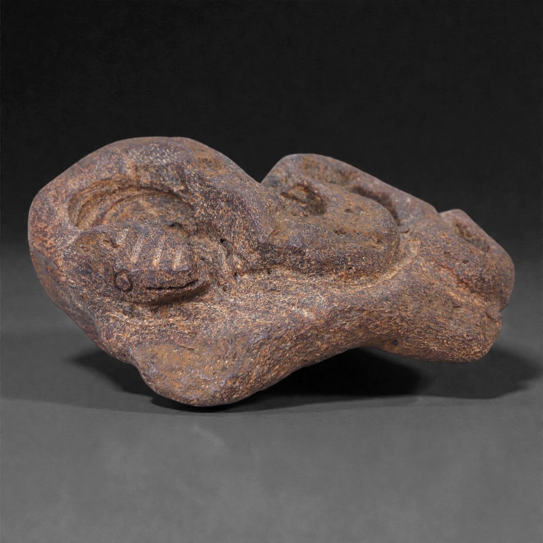 Ancient Fossil Bone Stone Snake Effigy - Zoomorphic Serpent Sculpture, 100Y: This compact zoomorphic effigy depicts a coiled snake, carved from dense fossilized bone stone and rendered in a restrained, archaic style. The serpent's body curves inward on itself, forming a low, s