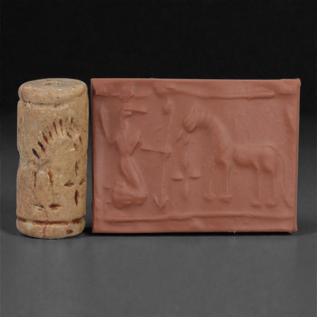 A Near Eastern Stone Cylinder Seal, 3rd Millennium BCE, 3.9cm, 45LM: Carved from stone with darker surface mottling, the cylindrical seal bears a continuous engraved scene. The carving is executed in shallow linear grooves typical of Early Bronze Age glyptic traditions