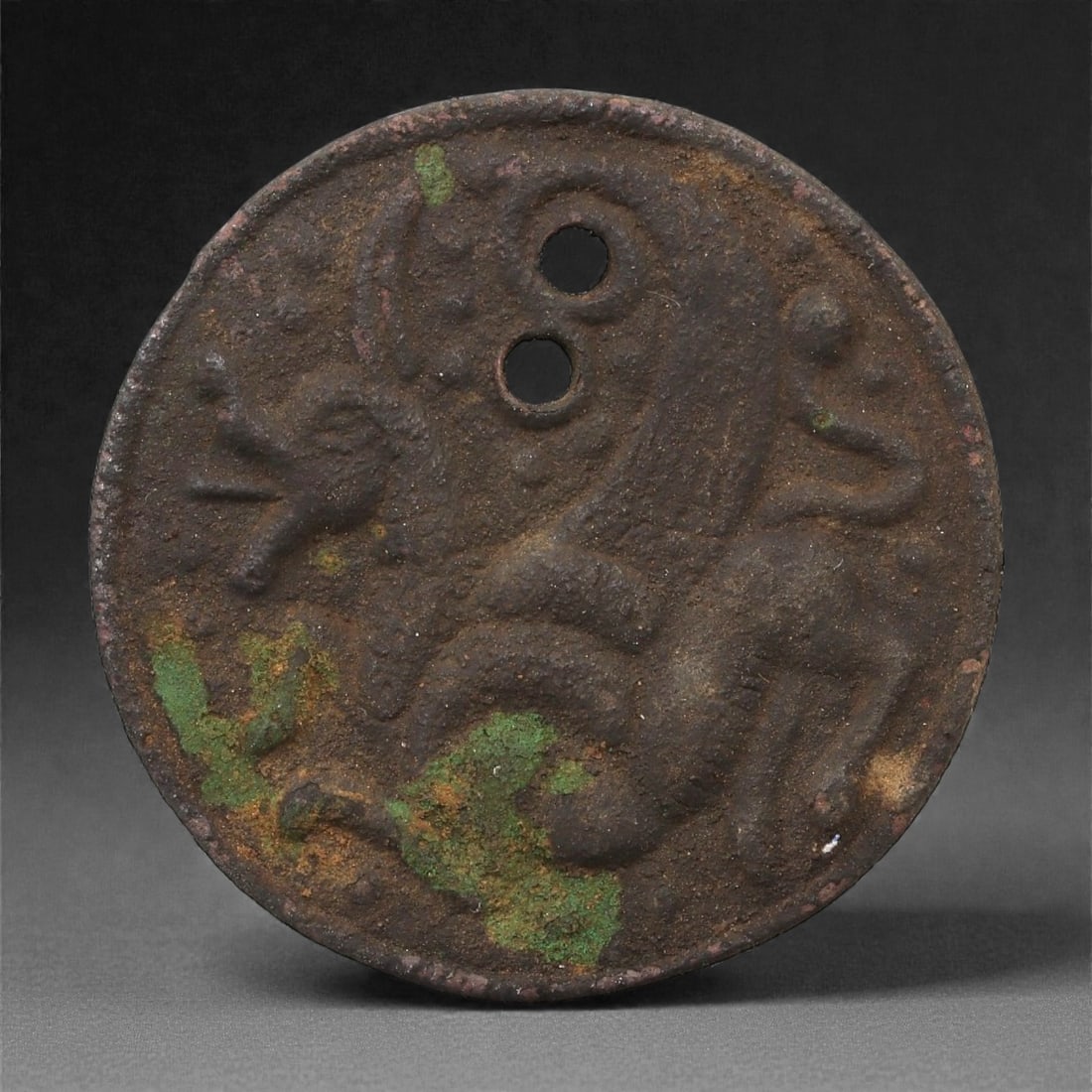 A Sasanian Bronze Medallion with Winged Hybrid, 3rd-6th Century CE, 54LP: Cast in bronze, the circular medallion bears a recessed depiction of a winged hybrid creature shown in profile. The body is modeled with rounded contouring, the head with a short projecting muzzle, an